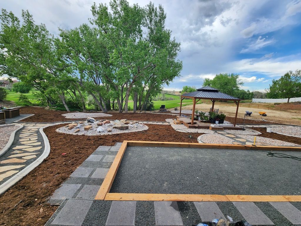 Backyard with stone paths, gravel play area, gazebo, and landscaped beds under a cloudy sky.