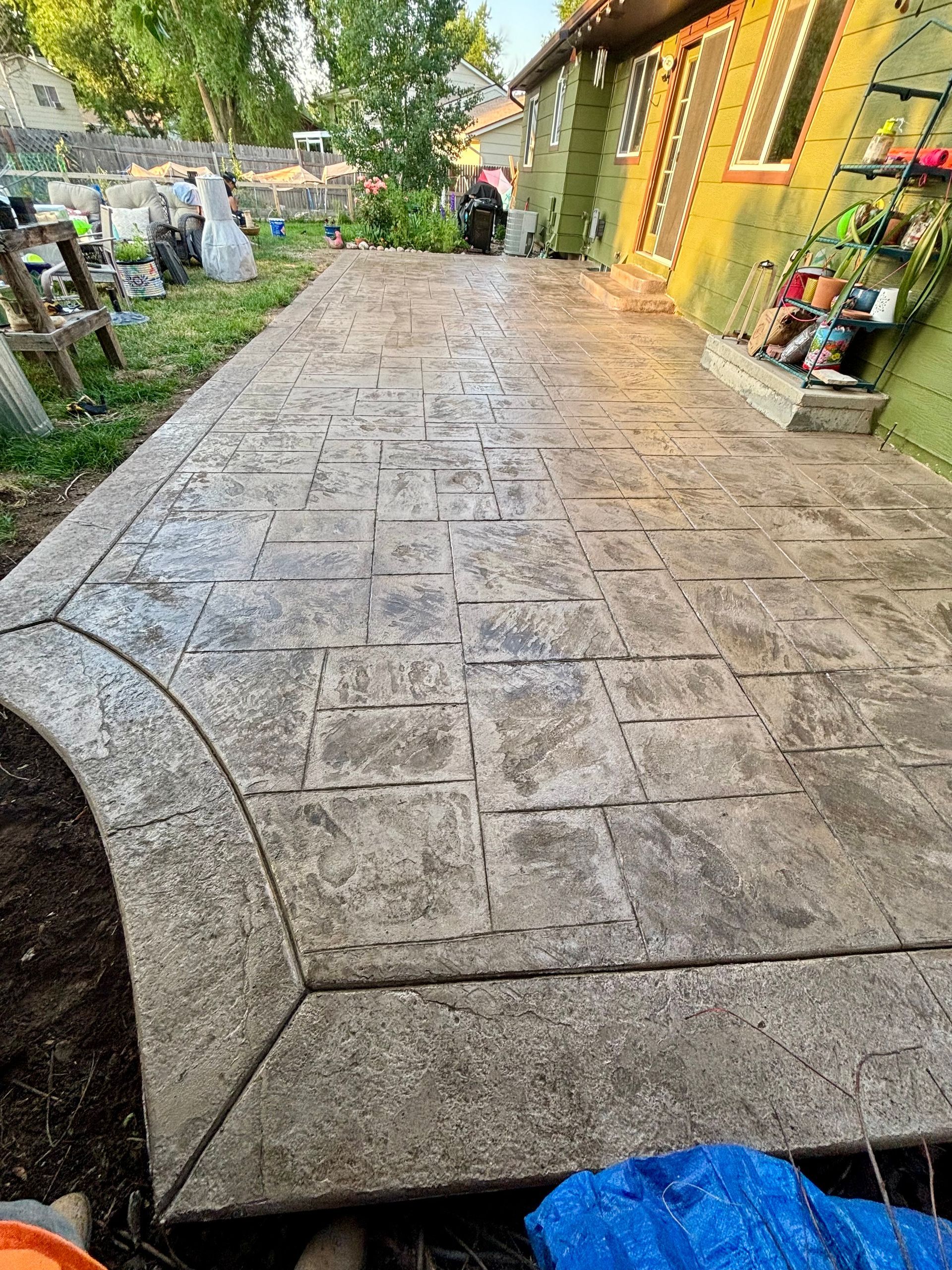 Stamped concrete patio with a curved edge next to a green house.