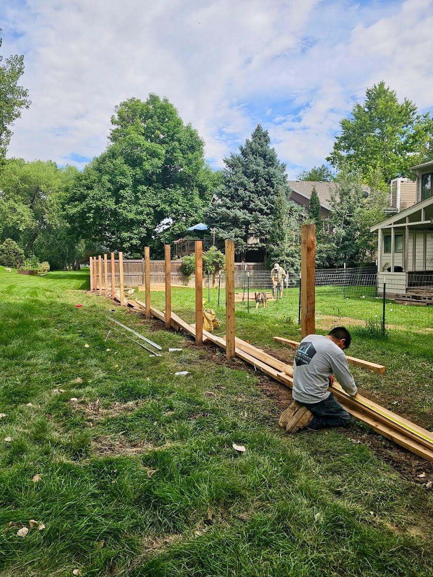 A person builds a fence on a grassy lawn with wooden posts and rails, sunny day.