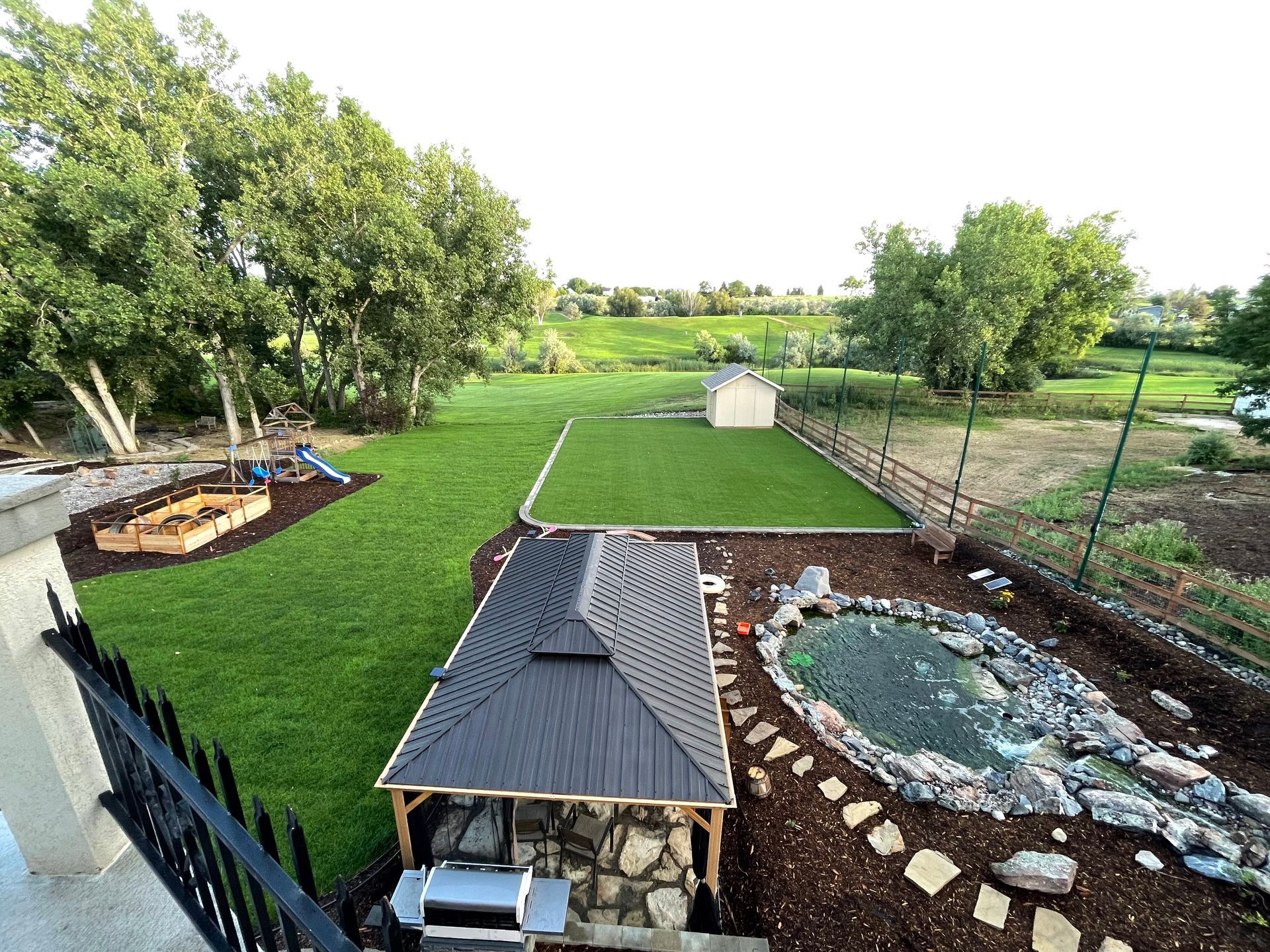 Backyard with gazebo, pond, play area, shed, and green lawn.