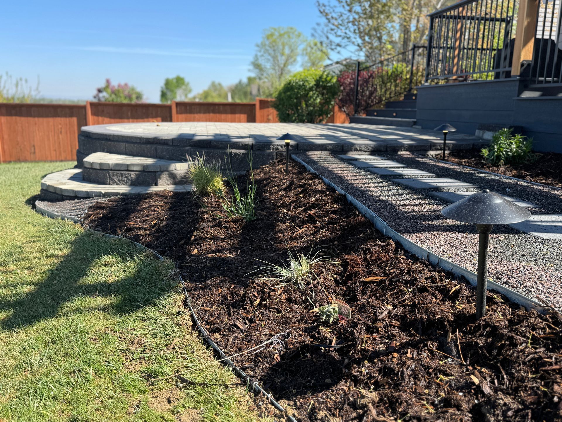 Backyard landscaping with steps, a patio, and a garden bed, with brown mulch and green grass.
