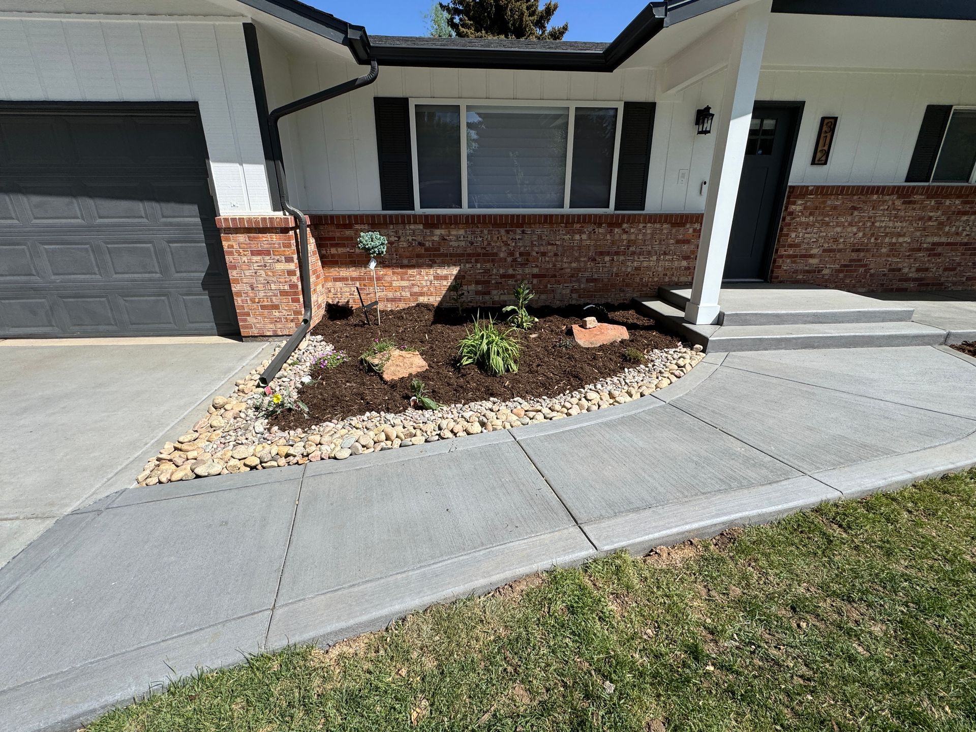 A house front with a concrete walkway, brick accents, and a landscaped garden bed.
