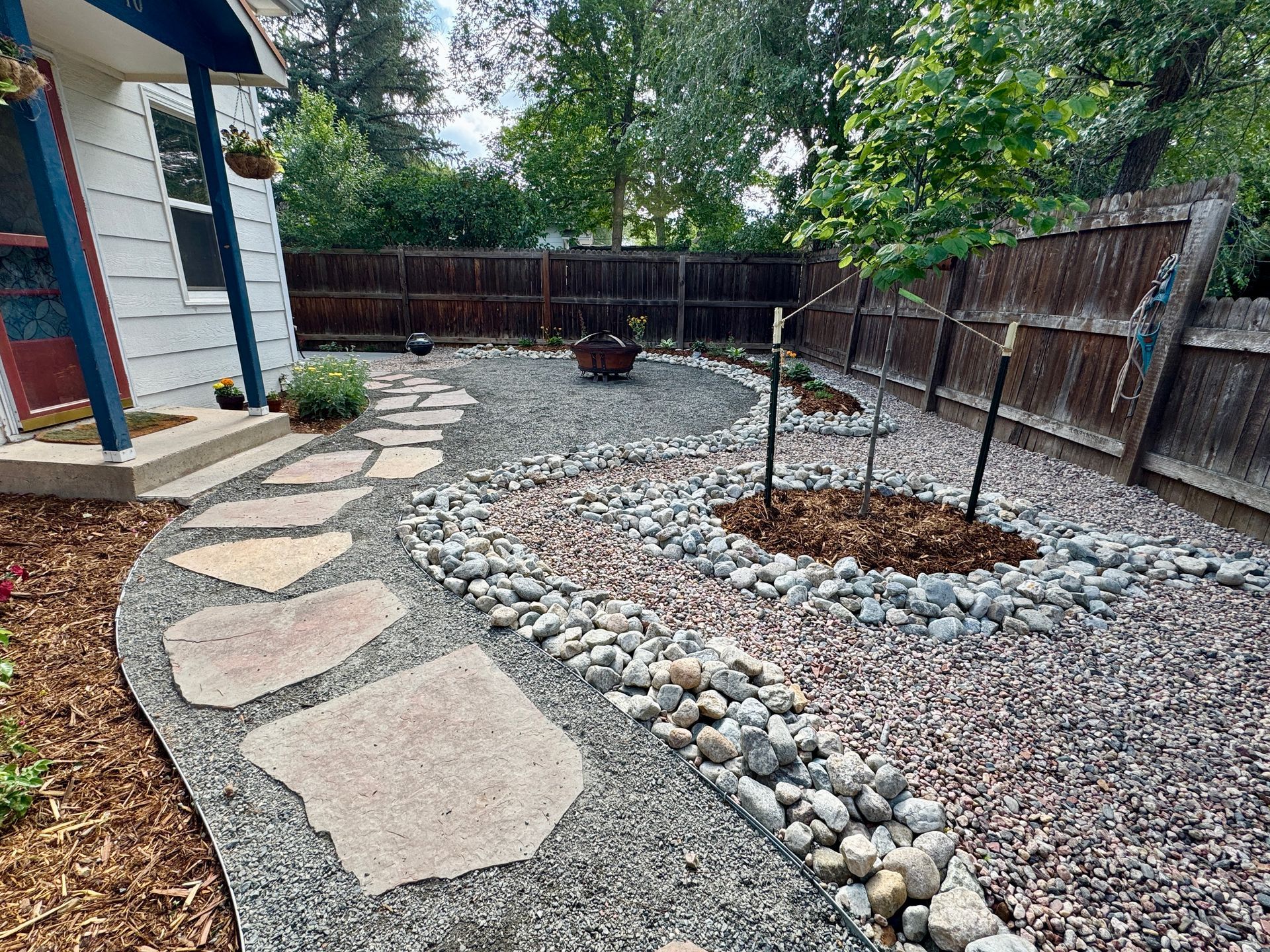 Stone path leads past a rock garden, fire pit, and fence in a backyard.