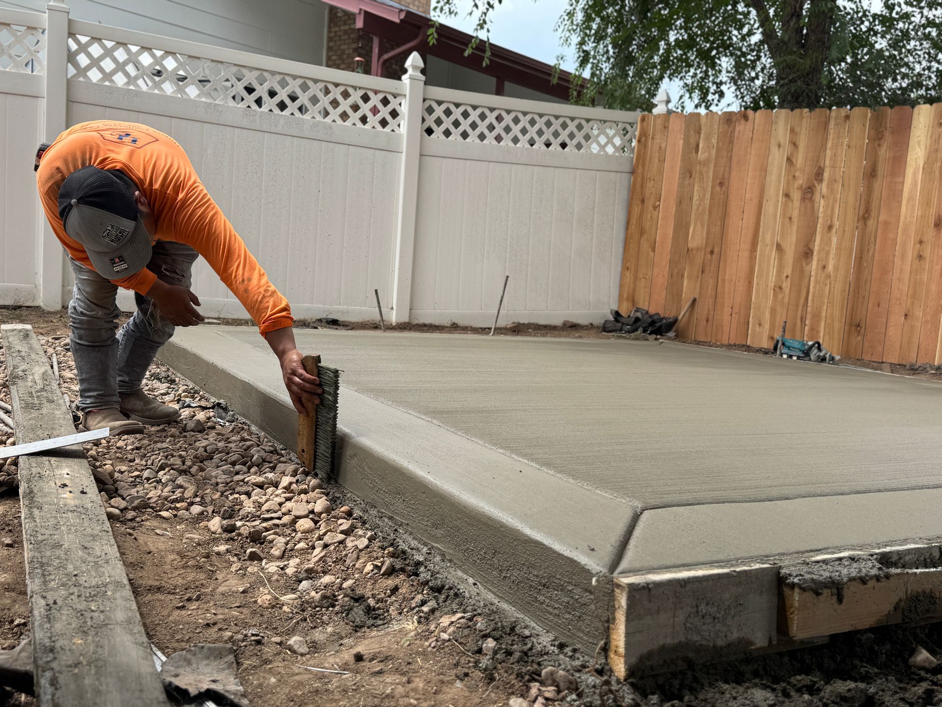 Construction worker leveling wet concrete slab in a backyard, using a wooden level tool.