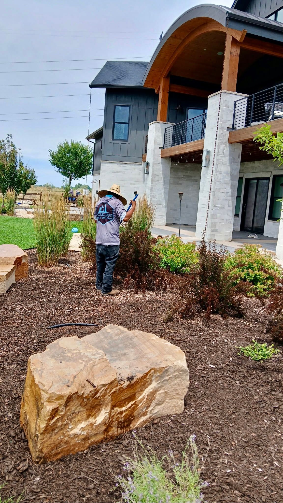 Gardener tending to plants in a landscaped yard next to a modern home.