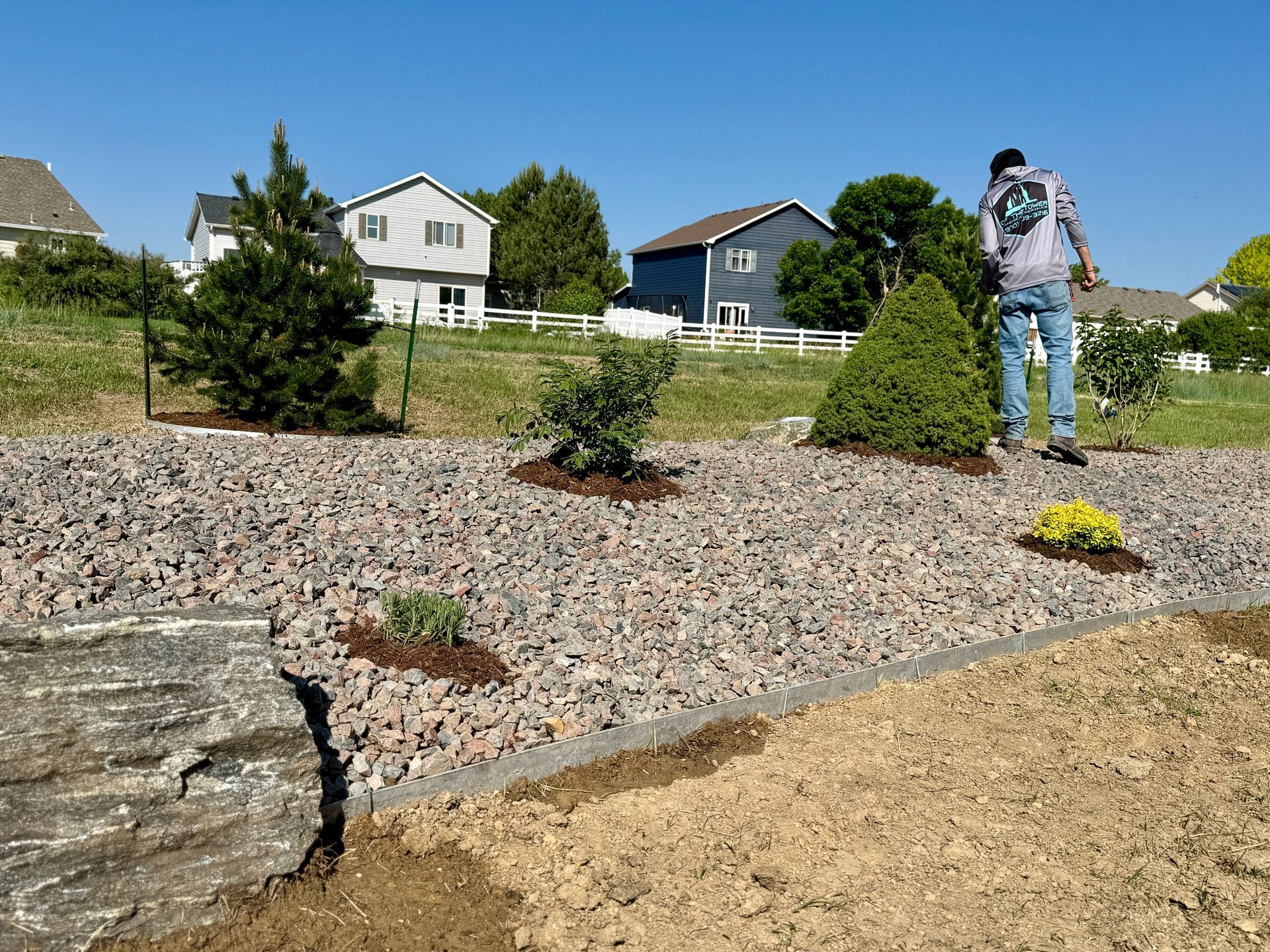 Man working in a rock garden near suburban houses; planting new flowers.