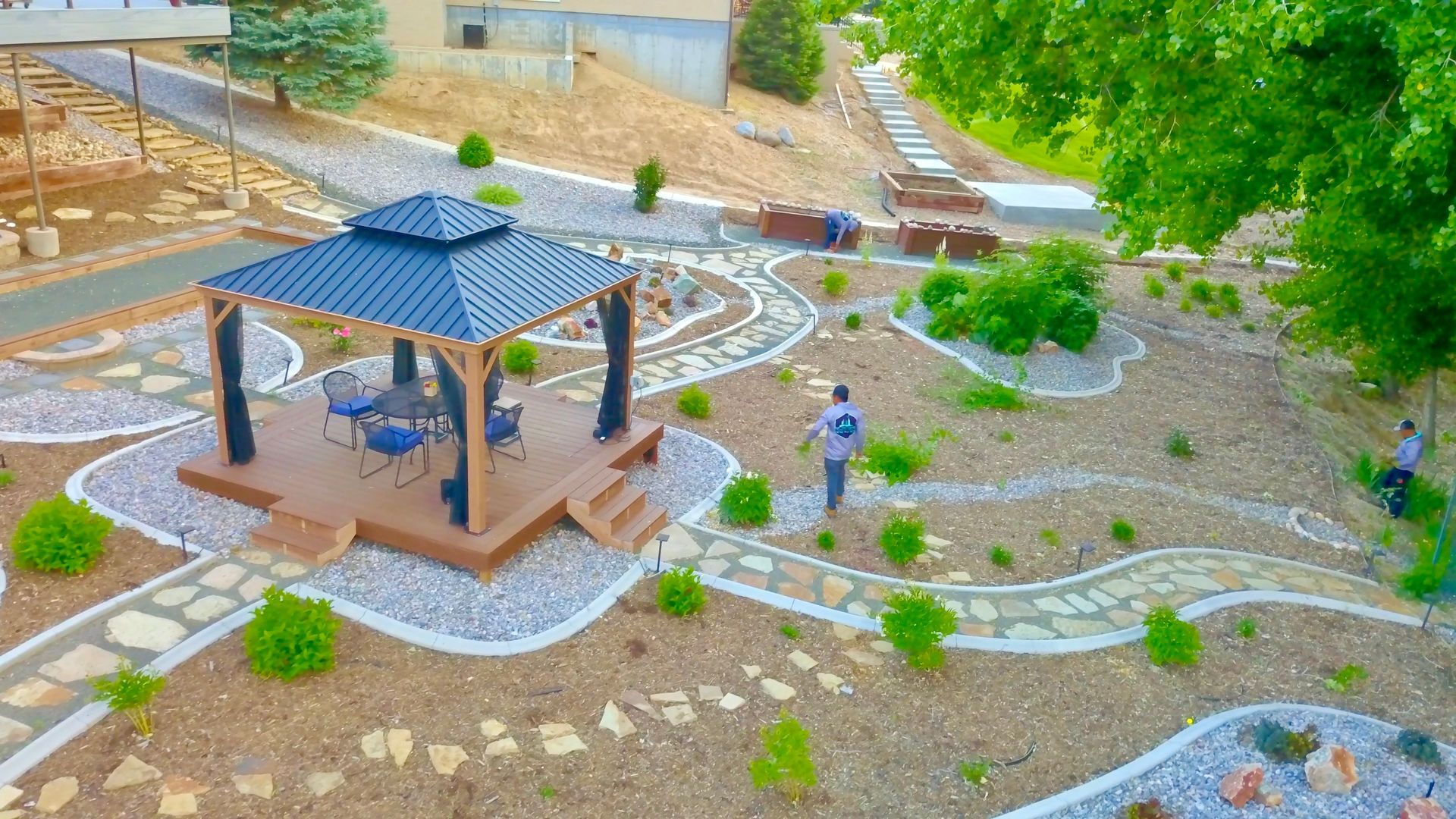 Gazebo with dining set in a landscaped garden with rock pathways, gravel, and small plants.