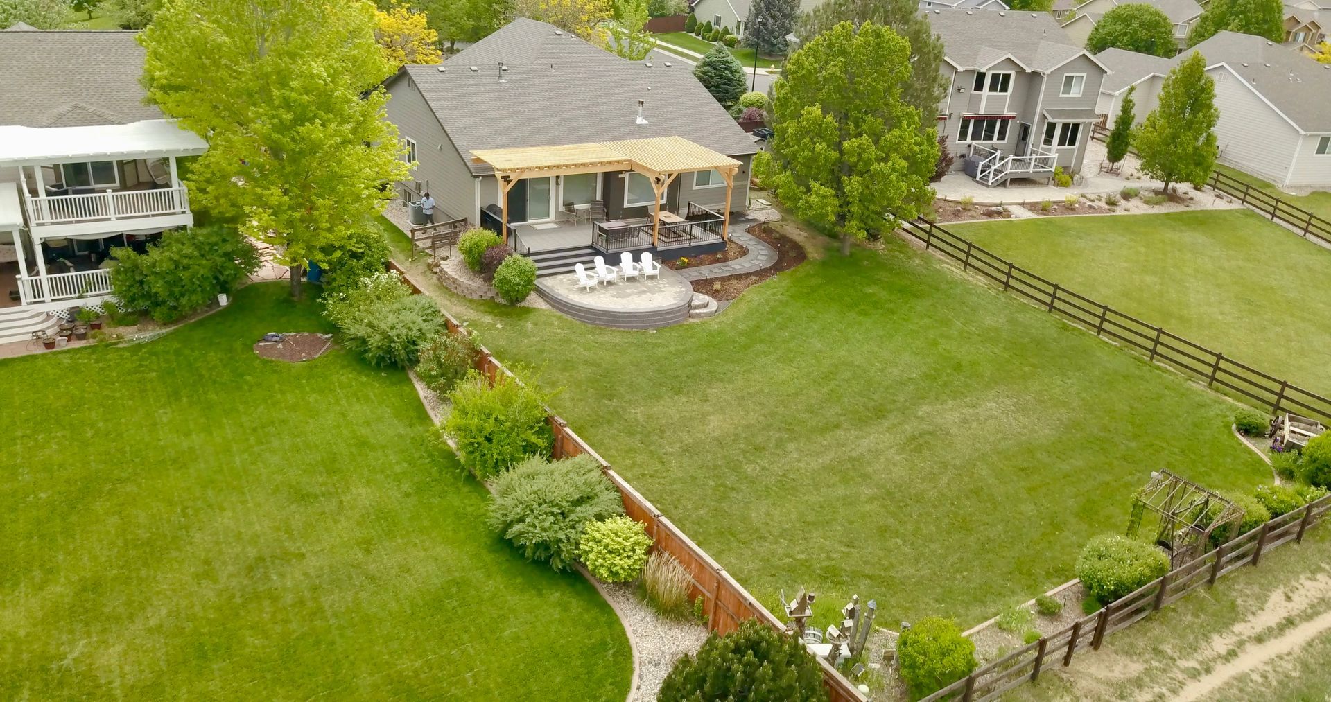 Aerial view of a suburban backyard with a house, patio, green lawn, fence, and landscaping.