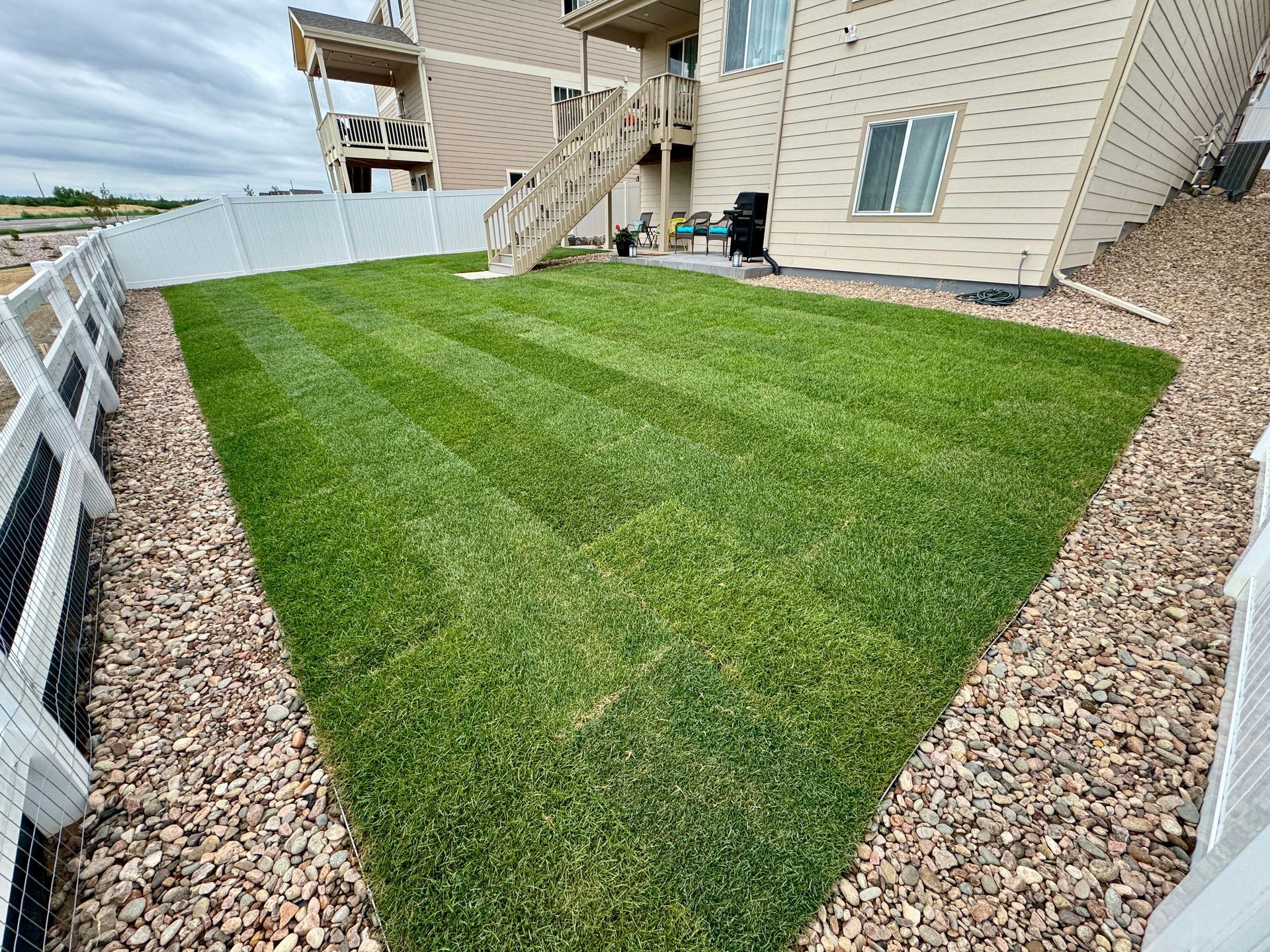 Freshly mowed green lawn bordered by a white fence and gravel, beside a two-story building.