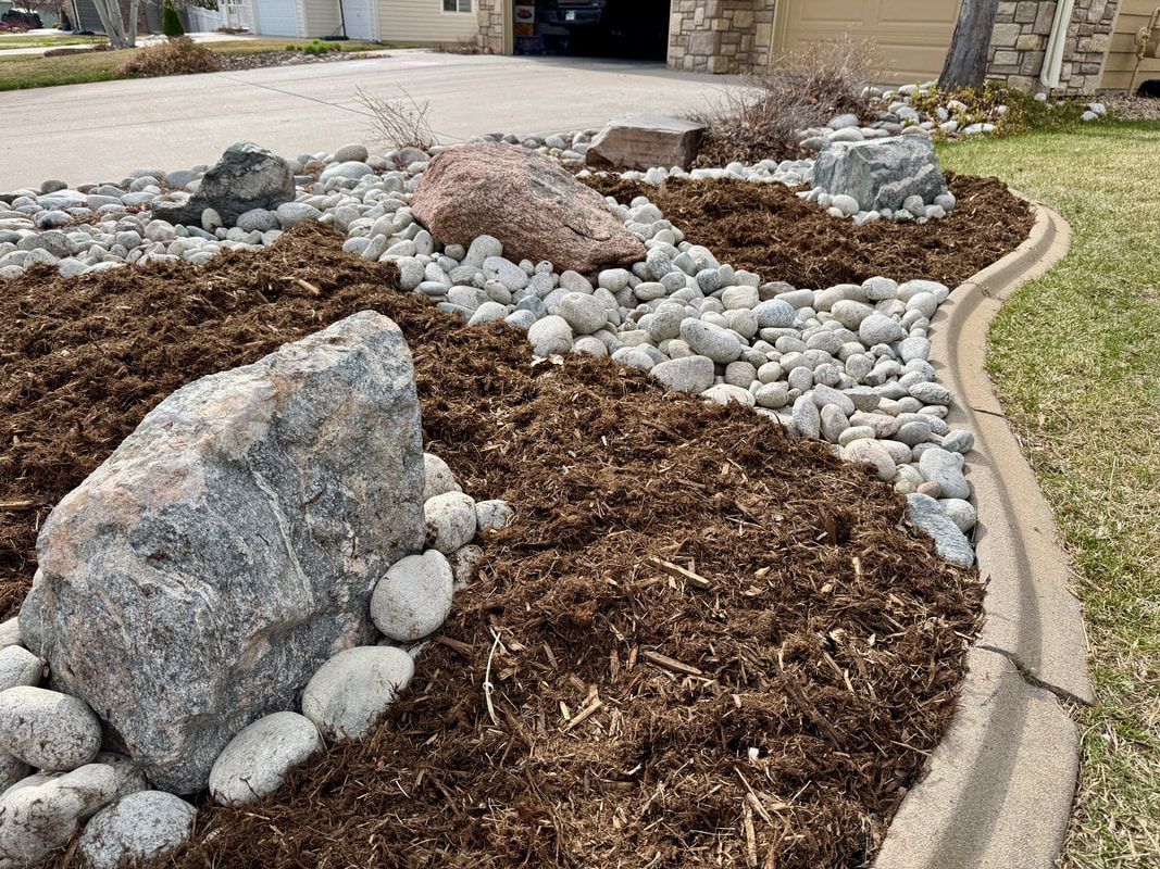 Rock garden with mulch, stones, and decorative edging along a driveway.