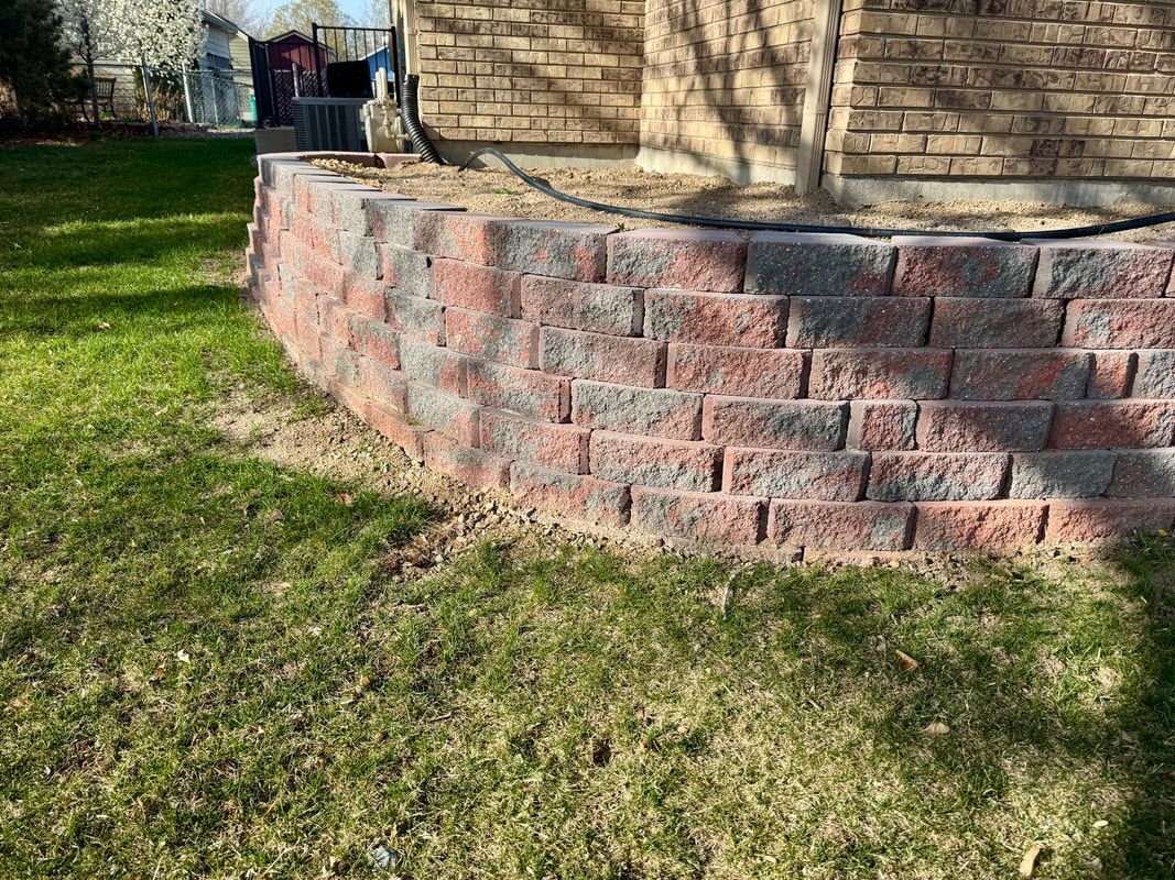 Red and gray brick retaining wall in front of a brick building and grass lawn.