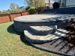 Stone patio with tiered steps, surrounded by grass and mulch. A wooden fence is in the background.