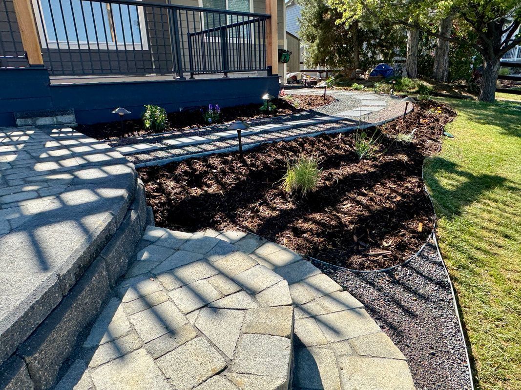 Stone walkway and landscaped flower bed beside a house with blue siding.