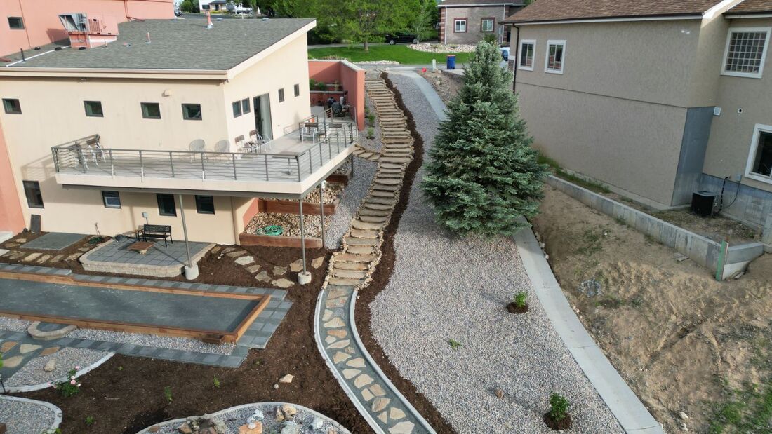 Residential backyard with stone pathways, stairs, deck, and landscaping.