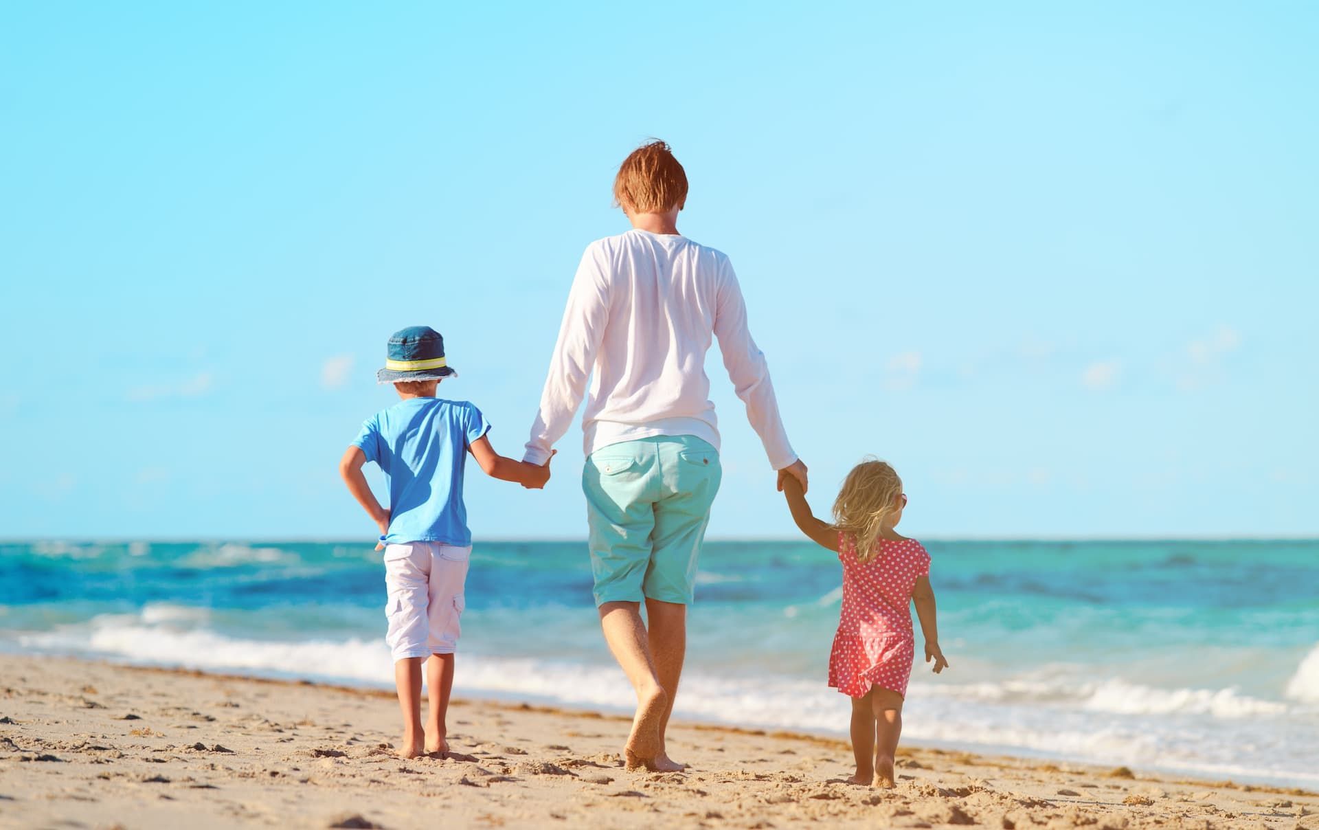 Three people holding hands and walking along a sunny beach by the ocean