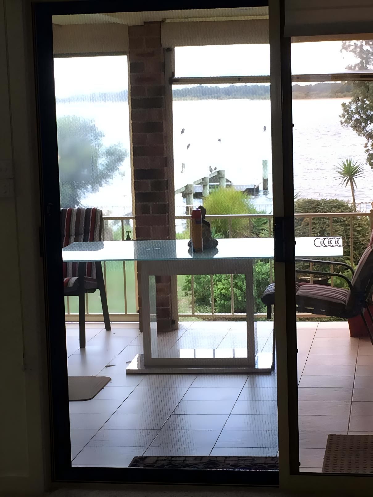 A Sliding Glass Door Leads to a Balcony With a Table and Chairs — Clearshield Security Screens in Shellharbour, NSW