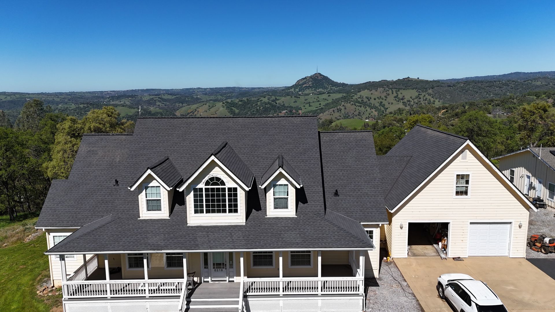 Large white house with dark roof, front porch, detached garage, and mountain view in the background