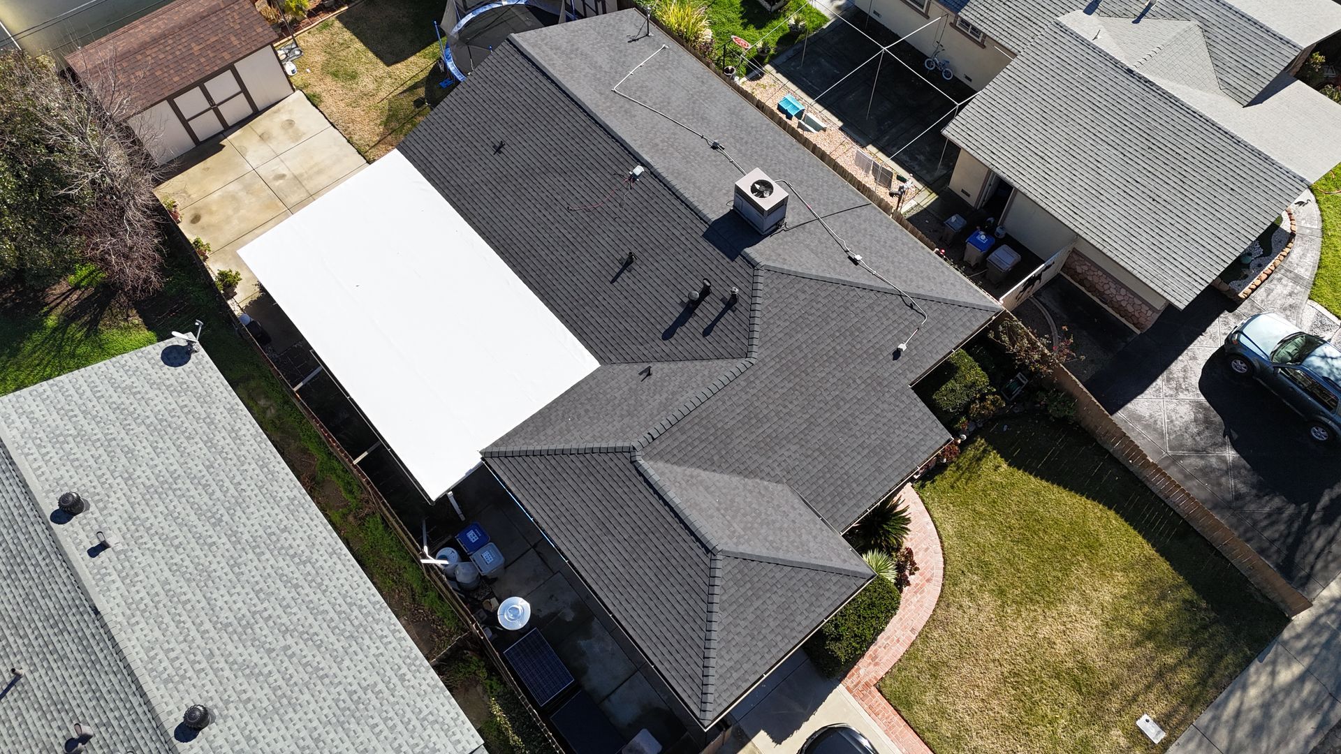 Aerial view of a house with a dark roof, white awning, and surrounding yard and neighboring homes.