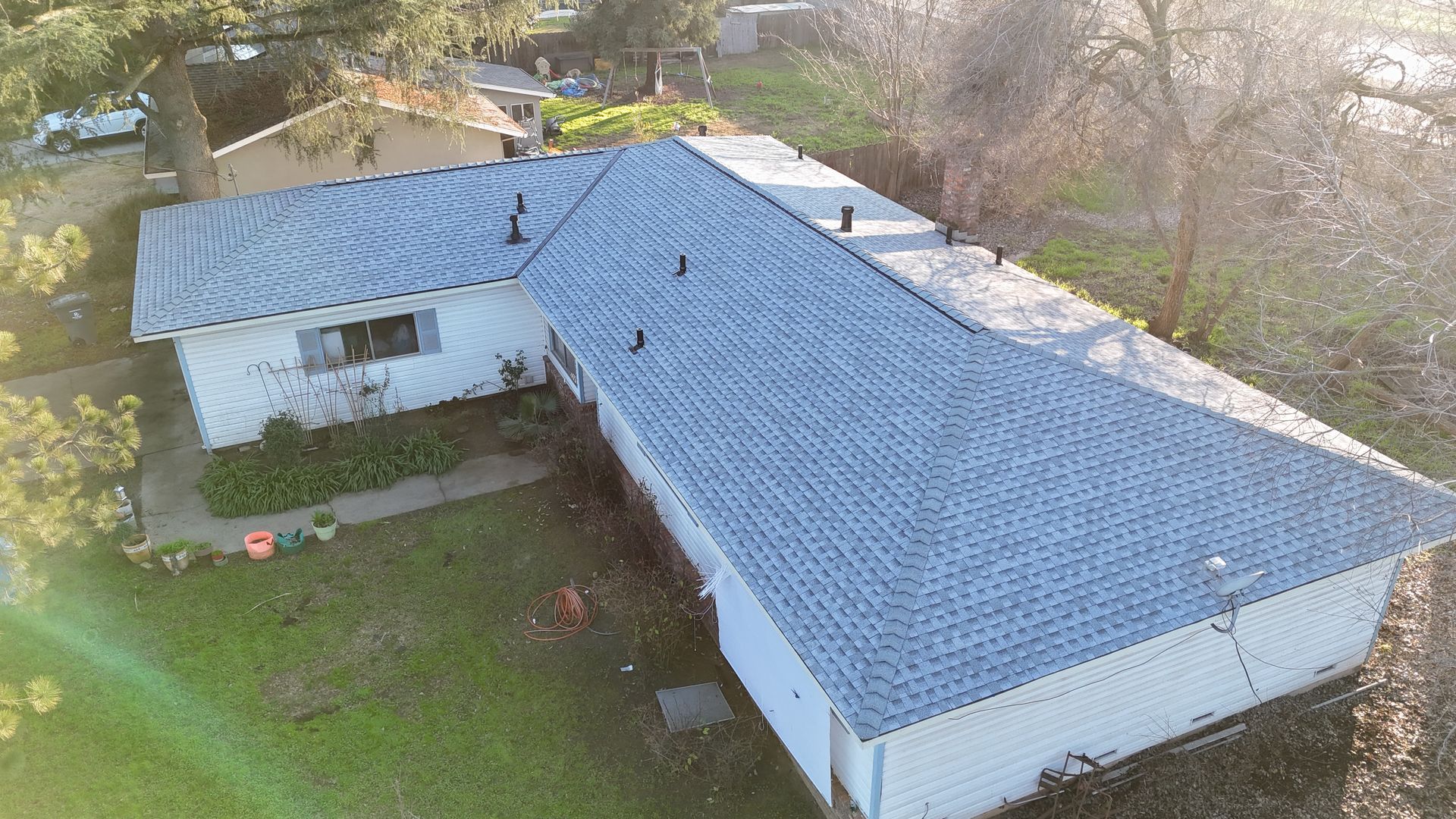 Aerial view of a white house with a blue roof surrounded by grass and trees.