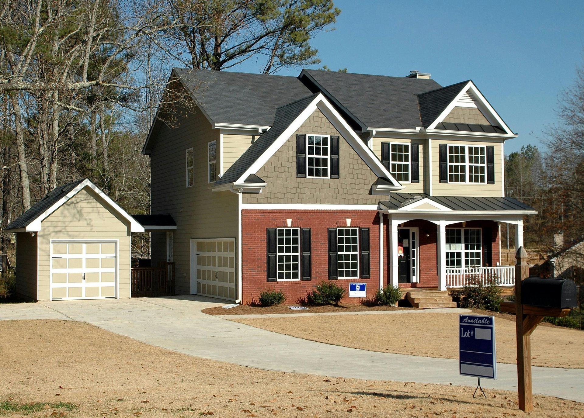 Two-story beige house with detached garage, red shutters, and front porch on a gravel driveway