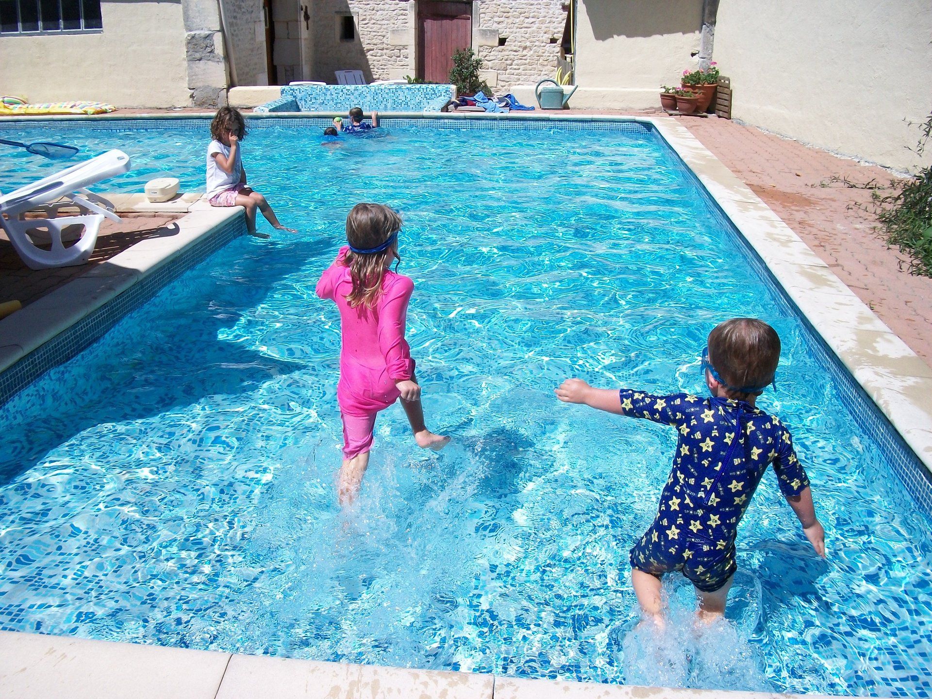 two young children wearing bright sun suits running into a shallow swimming pool