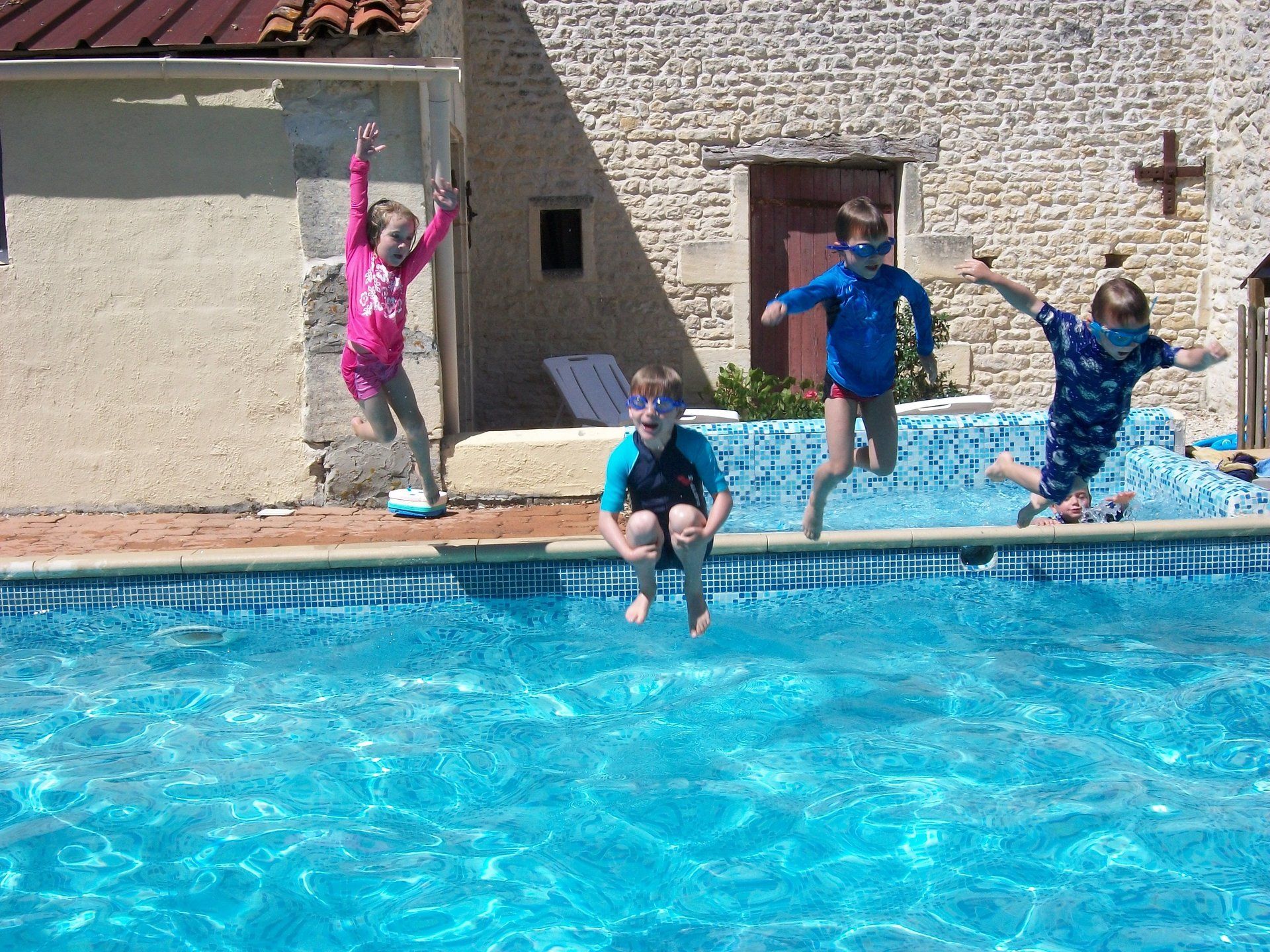four children jumping into a swimming pool waving their hands