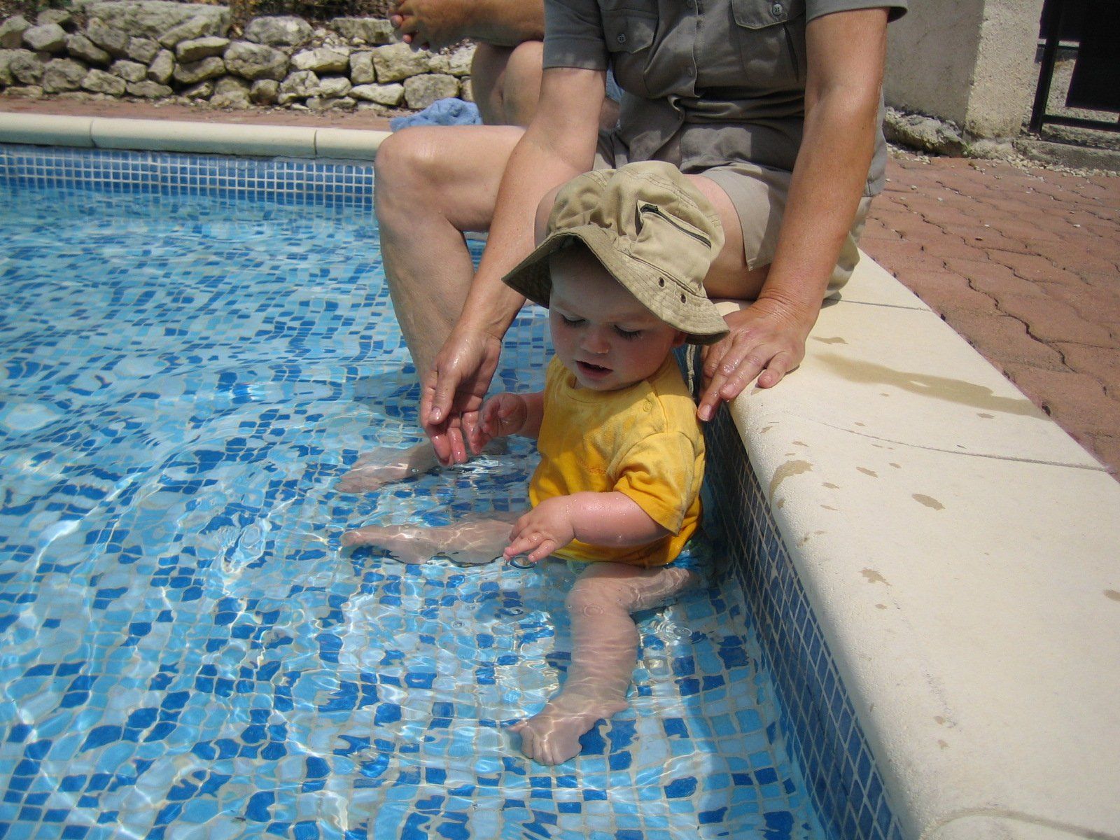 Toddler in yellow t-shirt paddling in a shallow swimming pool