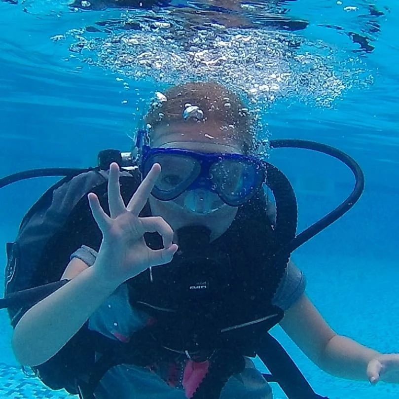 A child in scuba gear signaling OK to the camera under water