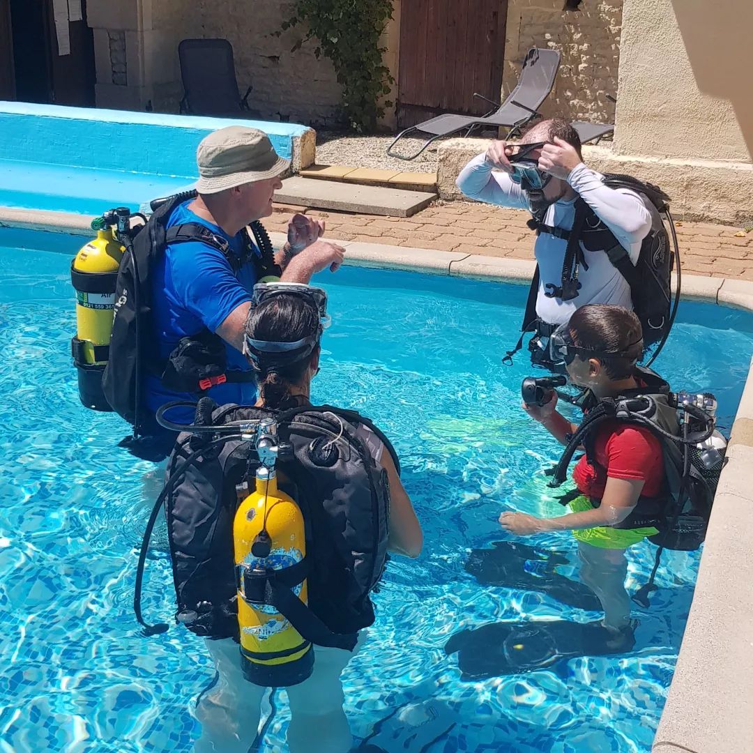 A scuba diving instructor teaching two adults and a child to scuba dive in a swimming pool