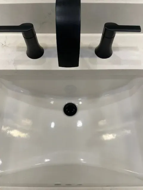 A bathroom sink with a black faucet and black handles.