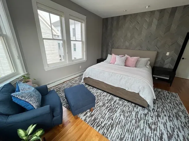 A bedroom with a bed , chair , ottoman and rug.
