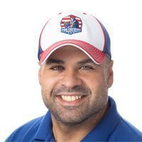 A man wearing a baseball cap and a blue shirt is smiling.