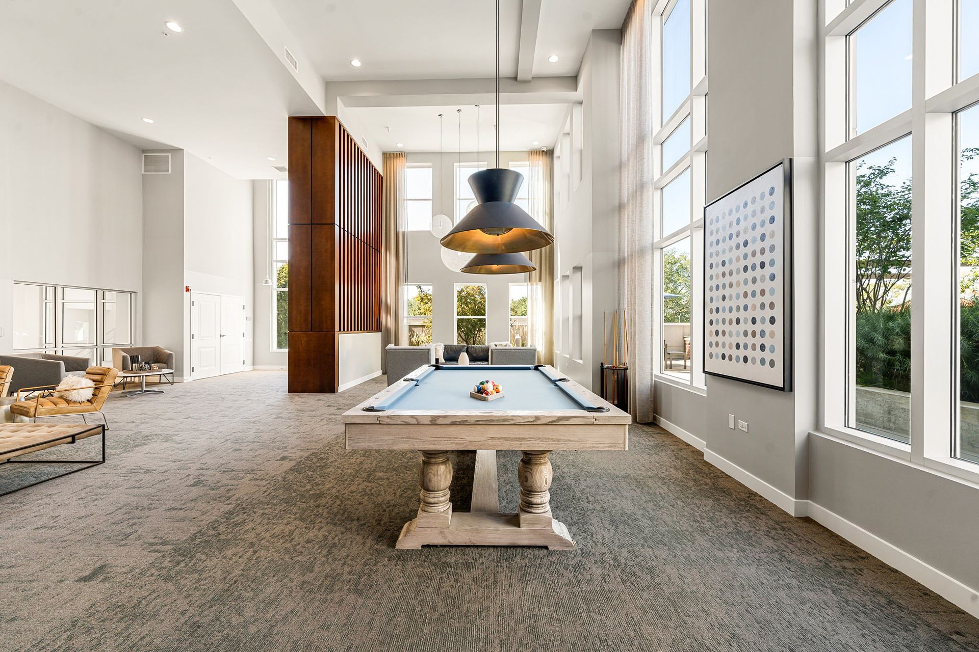 Pool table in modern lounge with large windows and decorative lighting.
