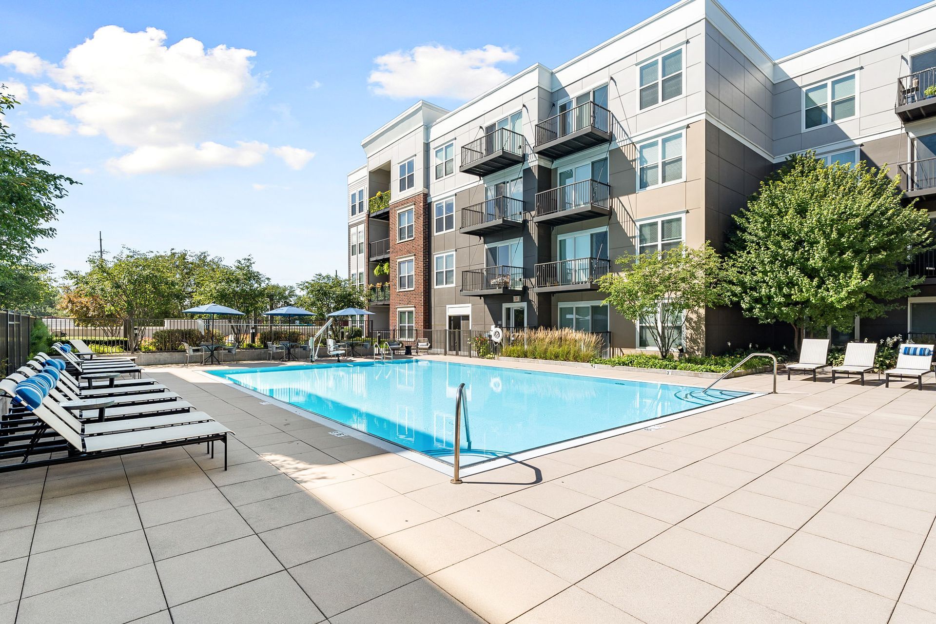 Apartment complex with a pool and lounge chairs; sunny day.
