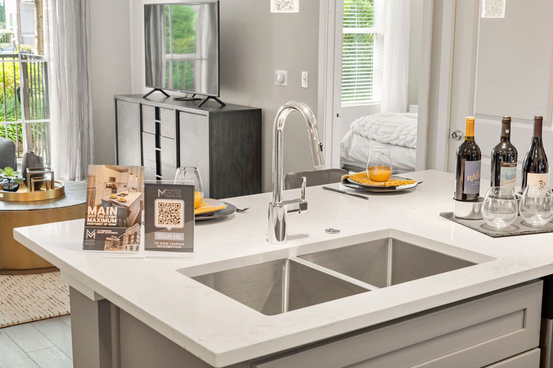 Kitchen island with sink, wine bottles, and a brochure; a TV and living area are visible.