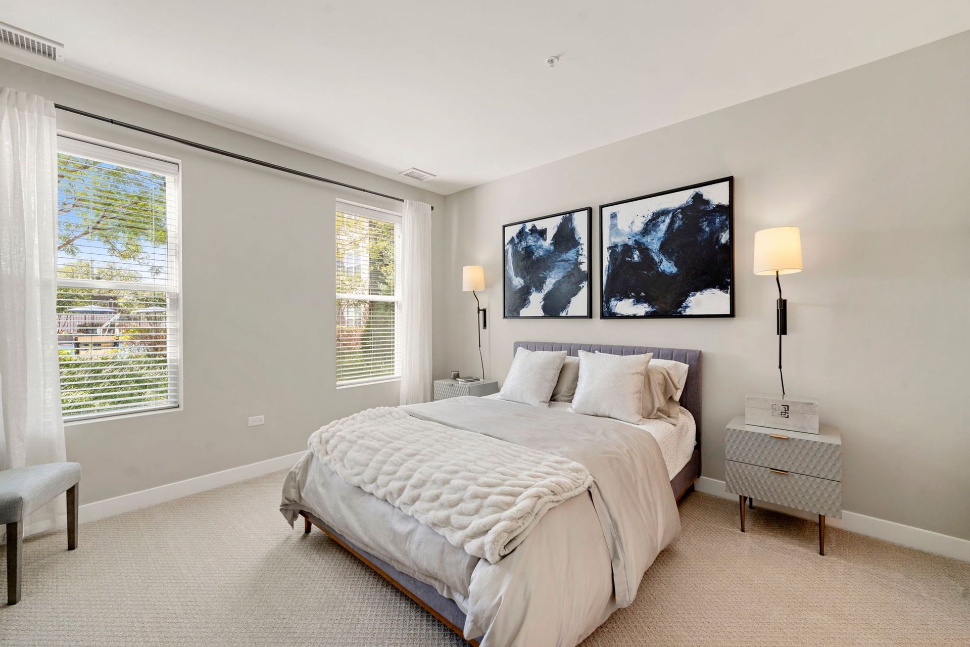 Bedroom with a bed, two windows, gray walls, and artwork.