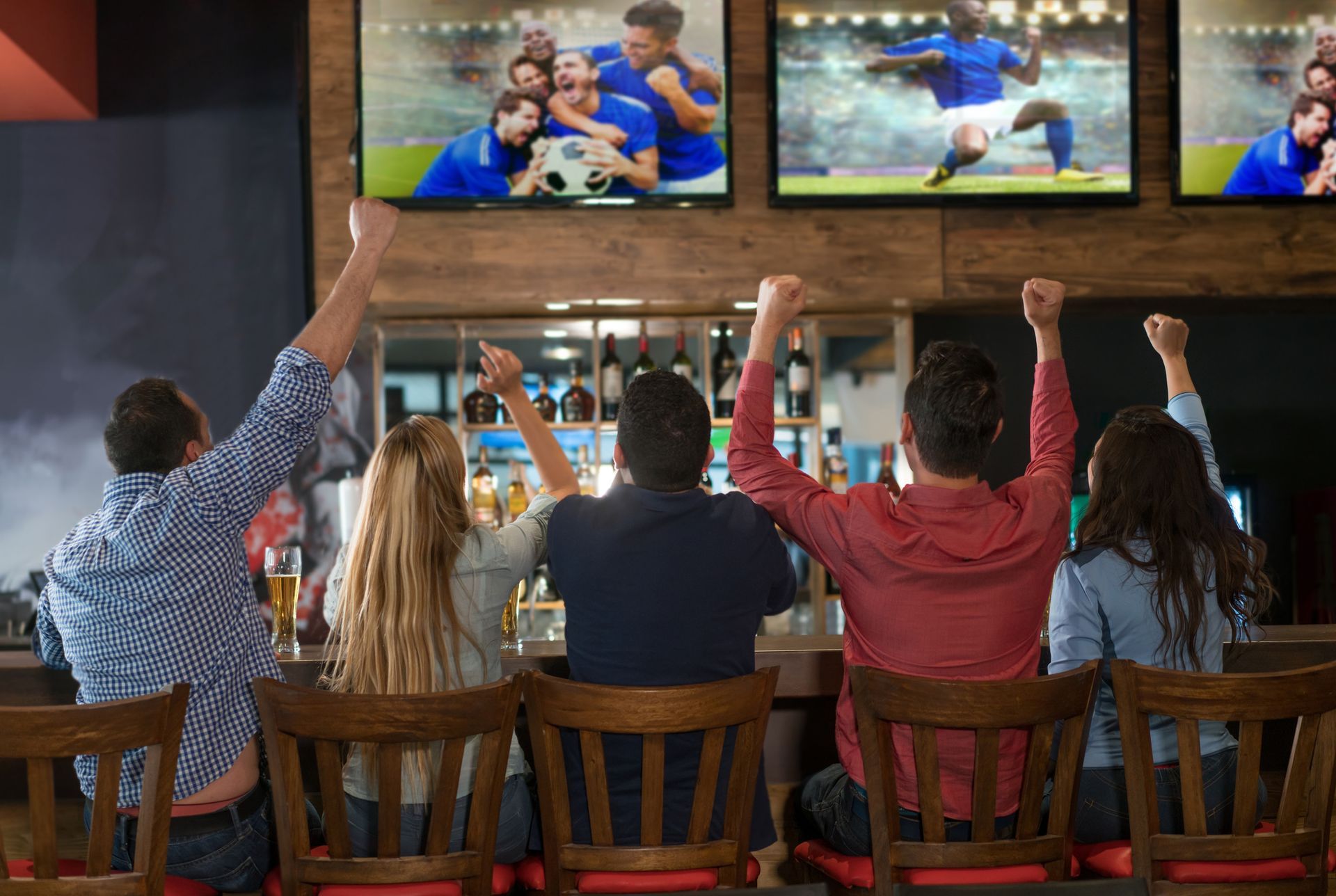 A group of people are sitting at a bar watching a soccer game on television.