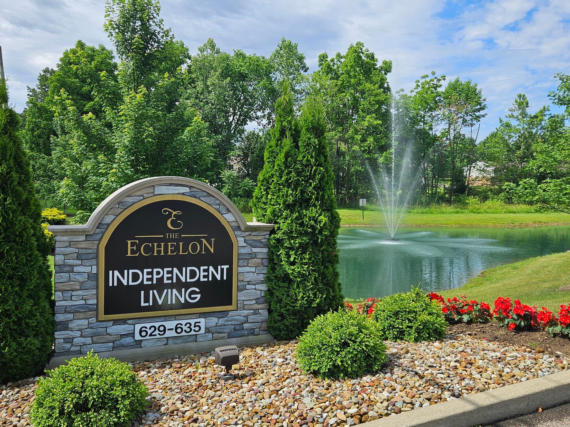 Sign for The Echelon Independent Living, featuring a pond and fountain, under a blue sky.