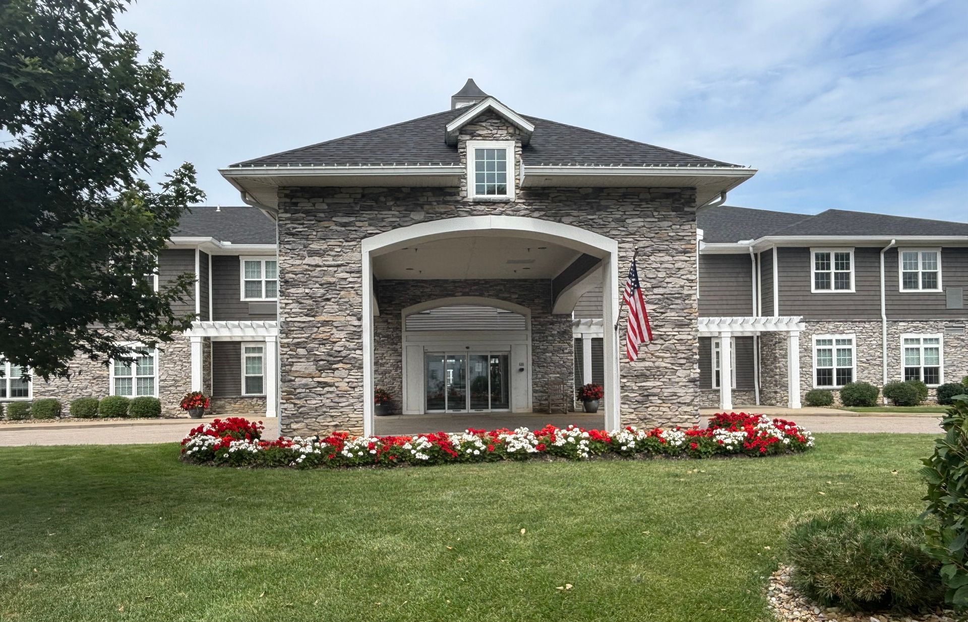 A stone-covered building with an entrance, an American flag, and flowerbeds.