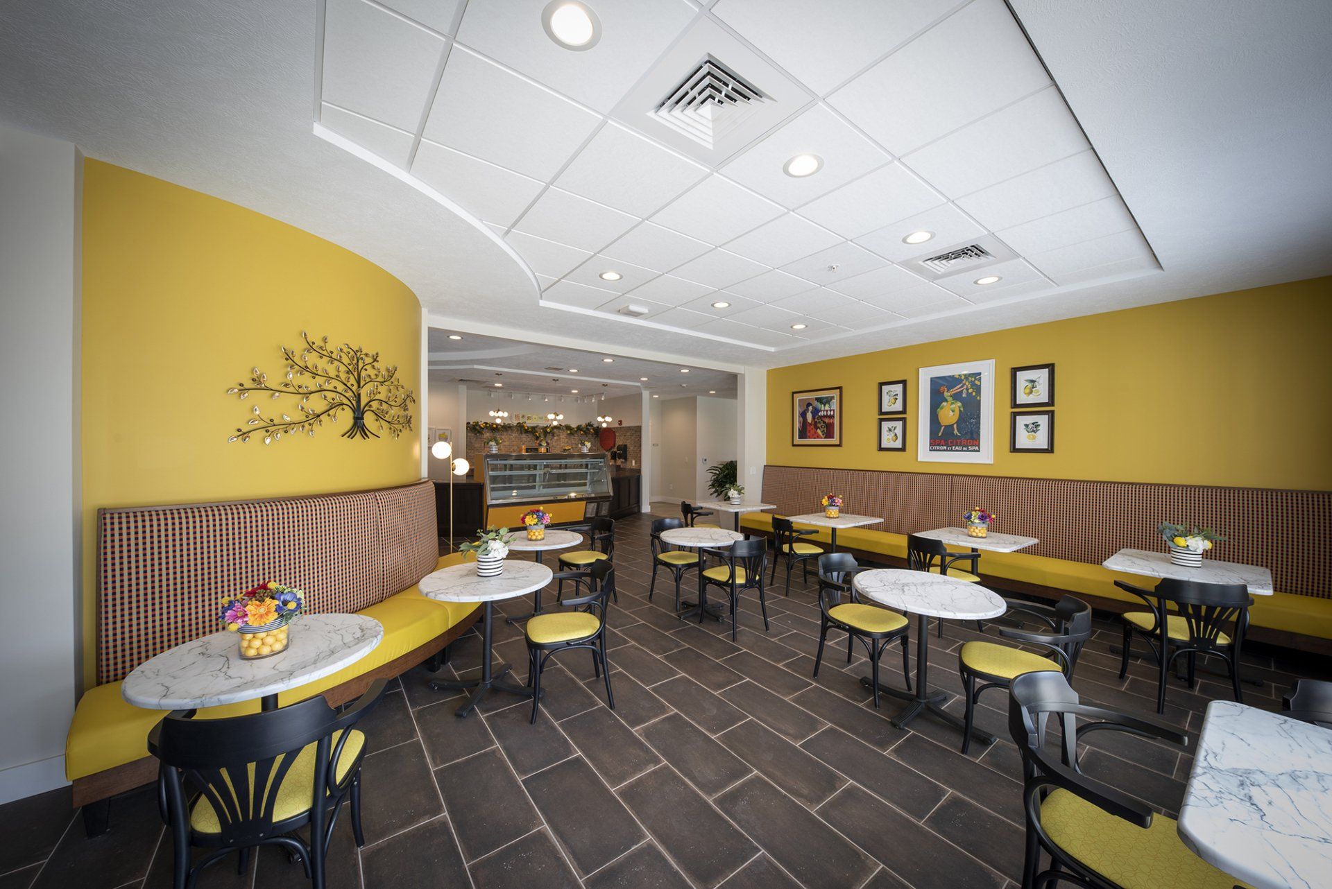 Cafe interior with yellow walls, round tables, black chairs, and a display case.