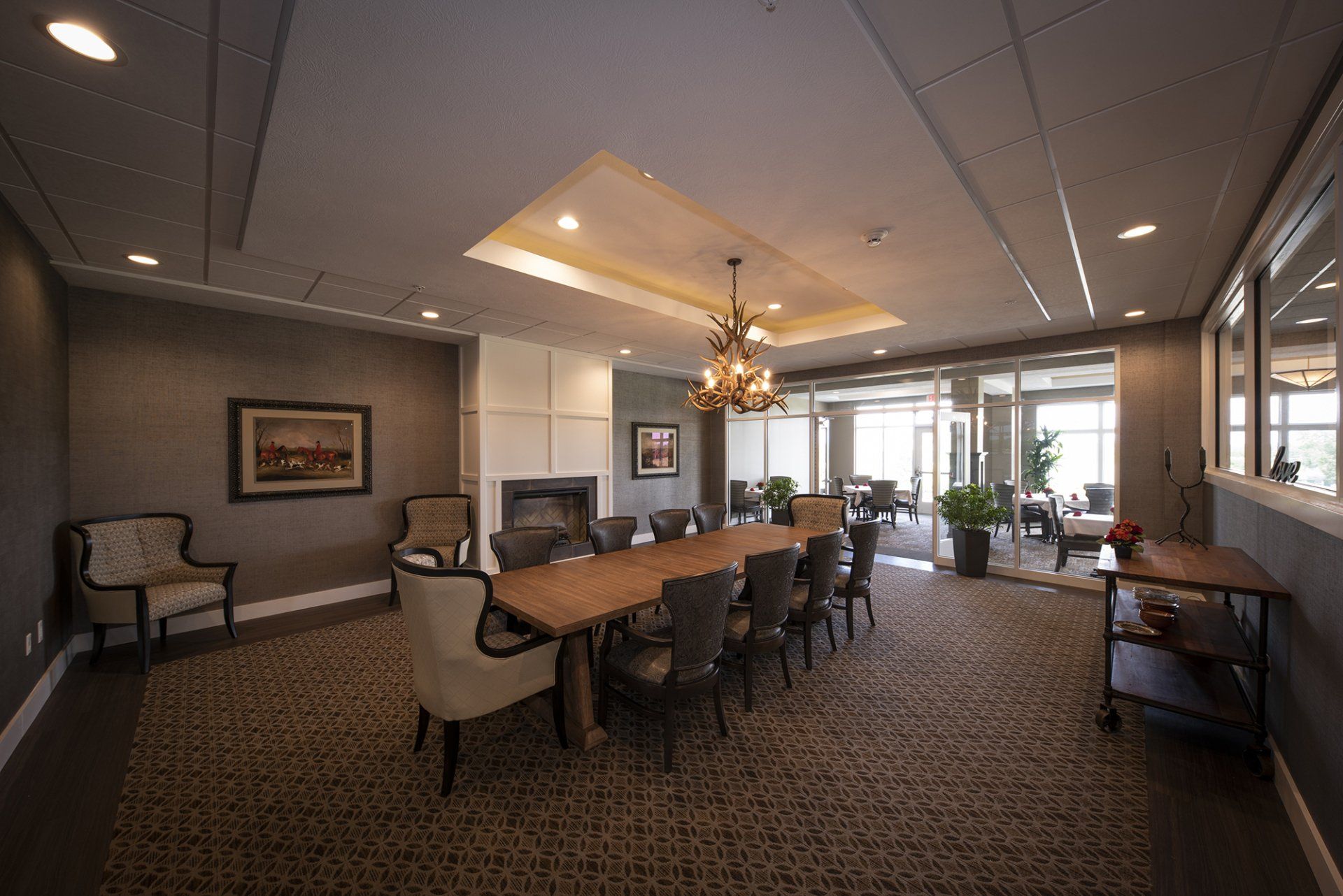A dining room with a long wooden table and chairs, fireplace, and a view outside.