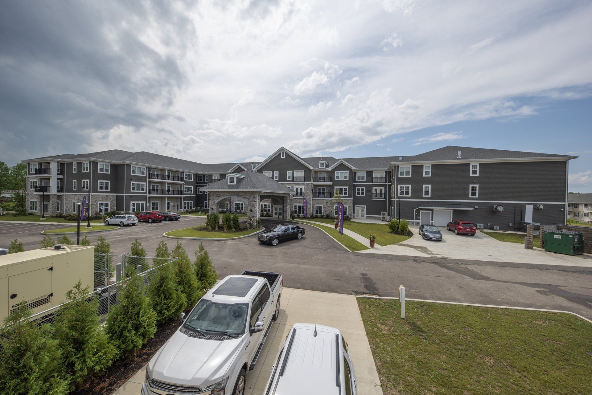Gray apartment building with cars in the parking lot and a cloudy sky.