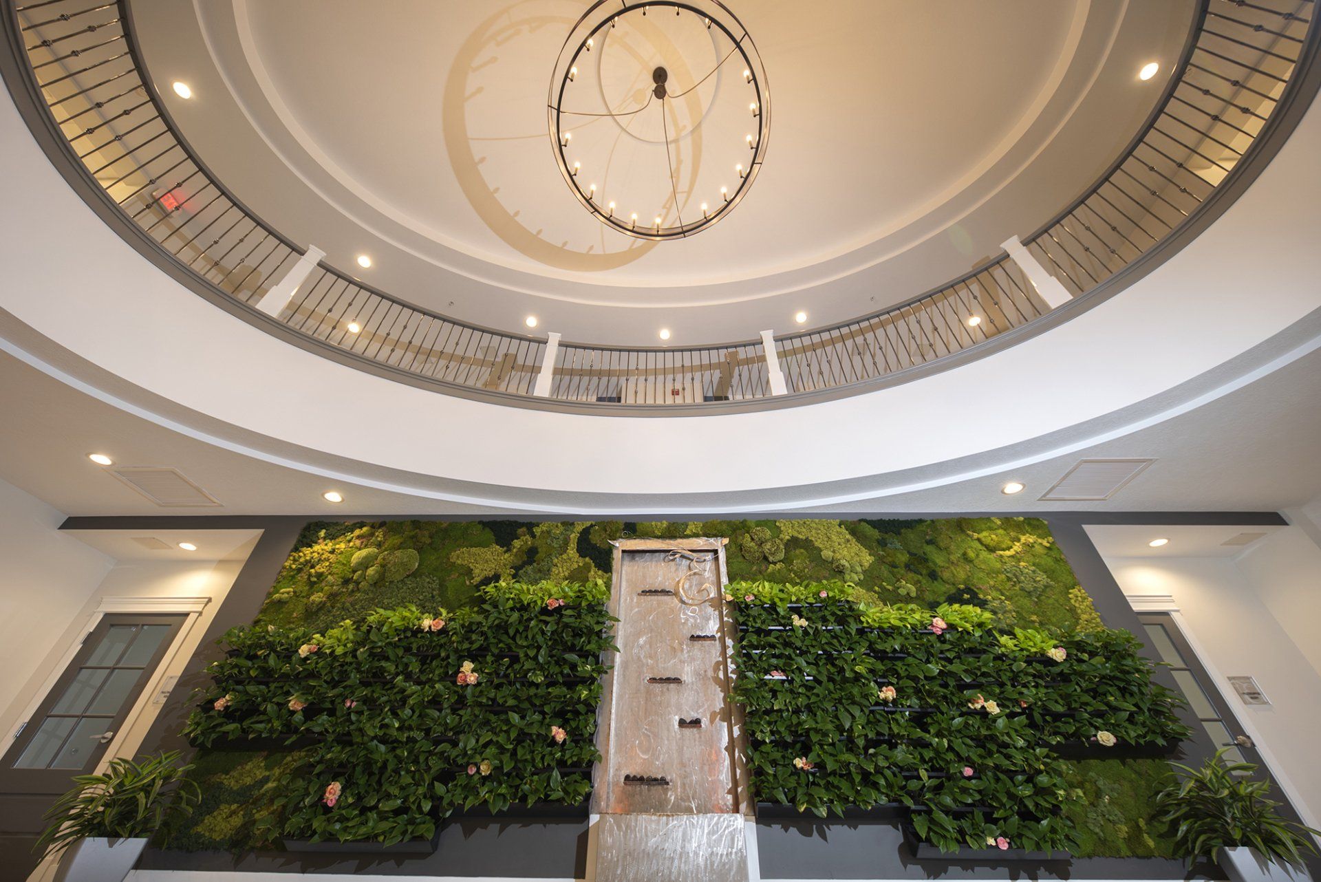 Foyer with a waterfall feature and living wall, under a balcony and large chandelier.