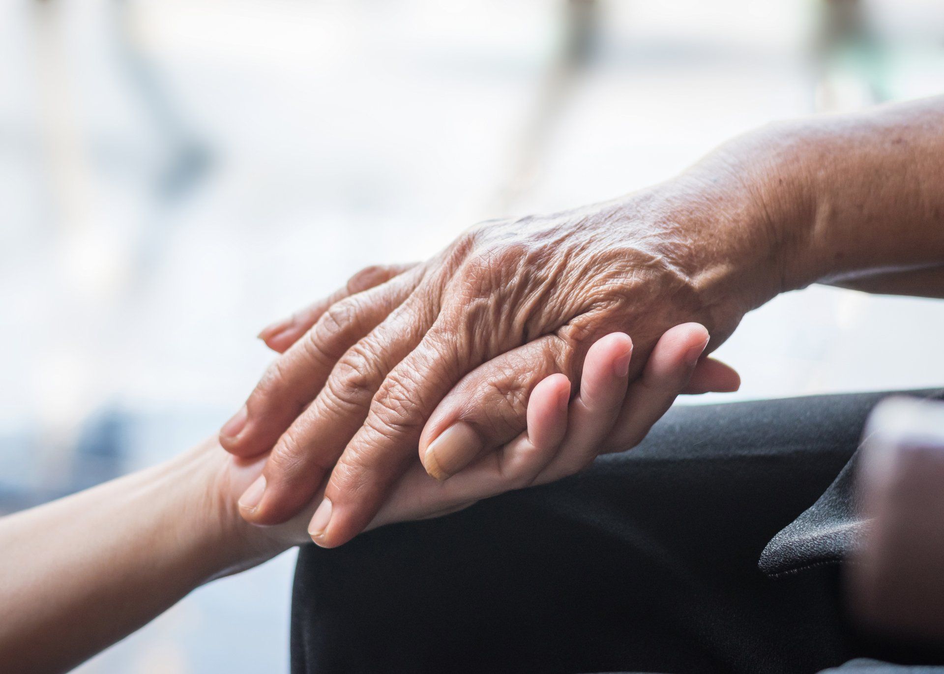 An older person's hand resting on a younger person's hand, symbolizing care and connection.