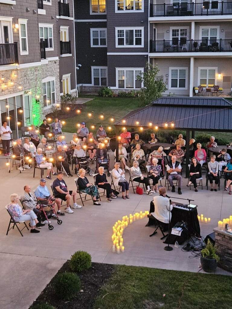 An outdoor gathering of seated people, lit by string lights and candles, near a building, evening.