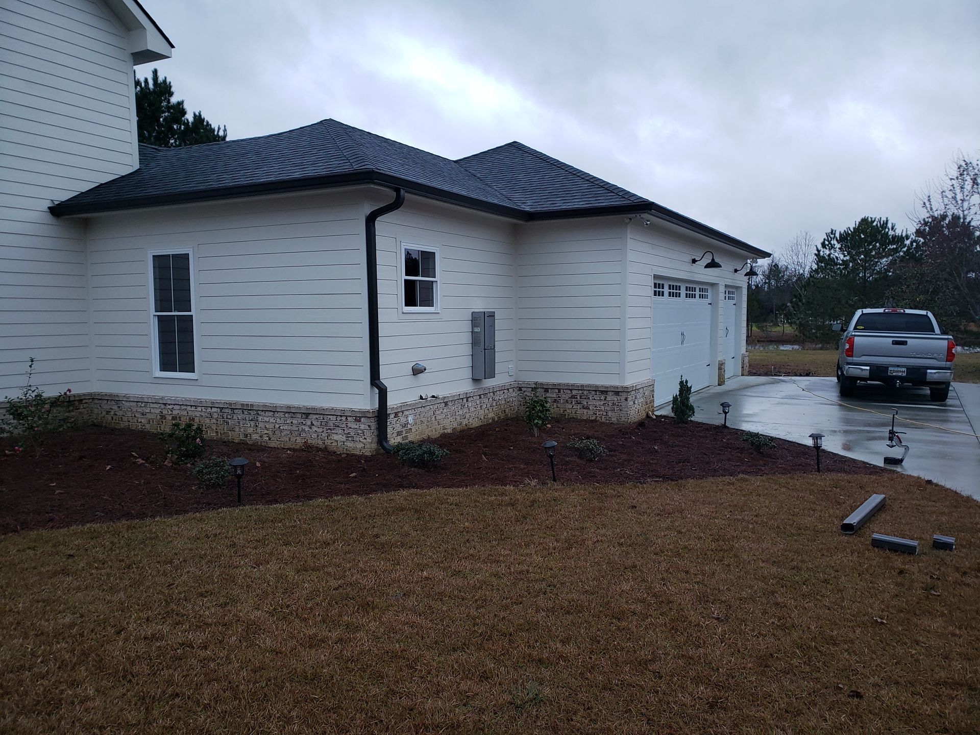 White house with dark roof and garage, stone accent on base, silver truck parked in driveway.