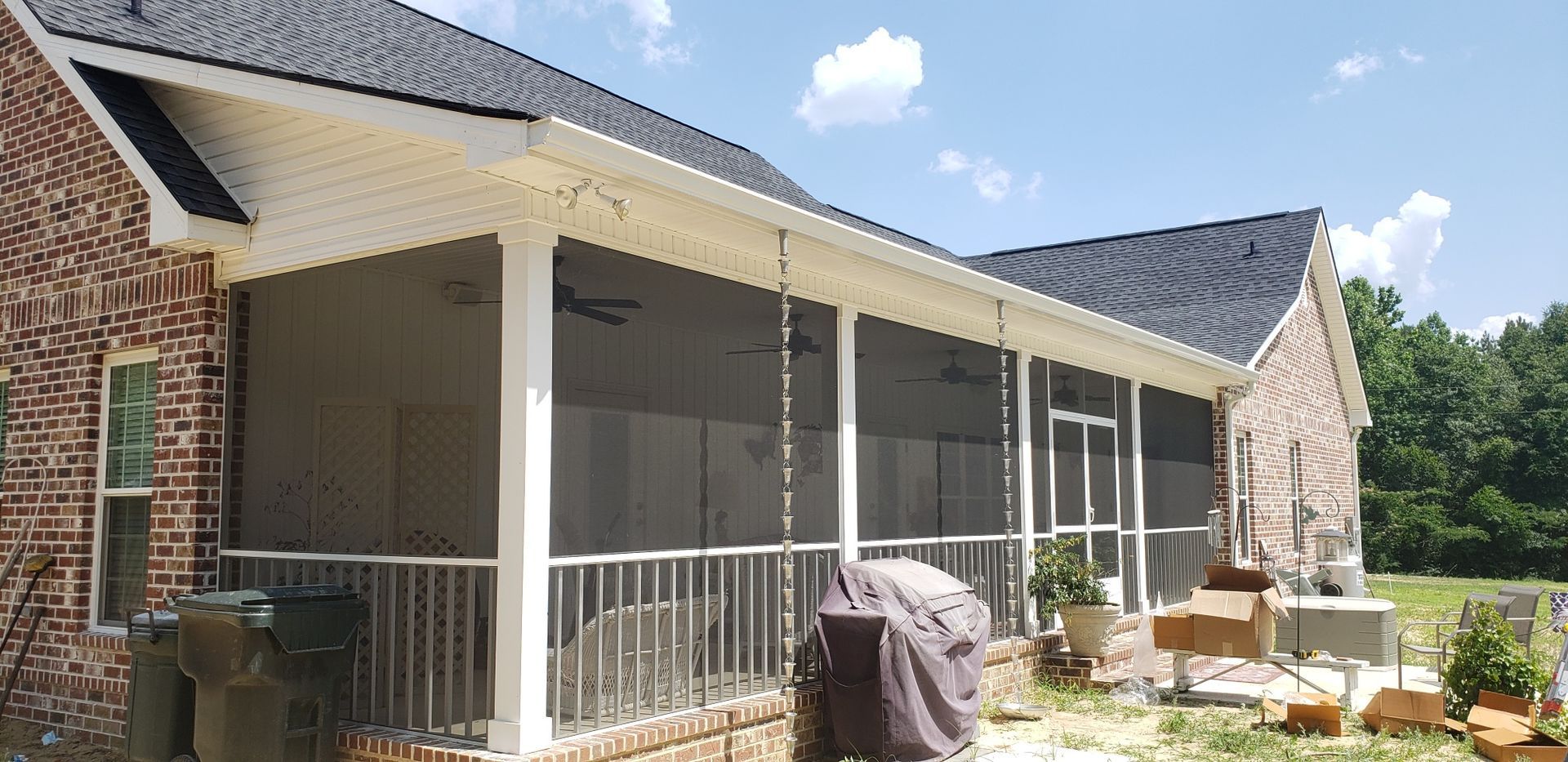 Screened-in porch on a brick house. White railing and trim, black roof. Sunny day.