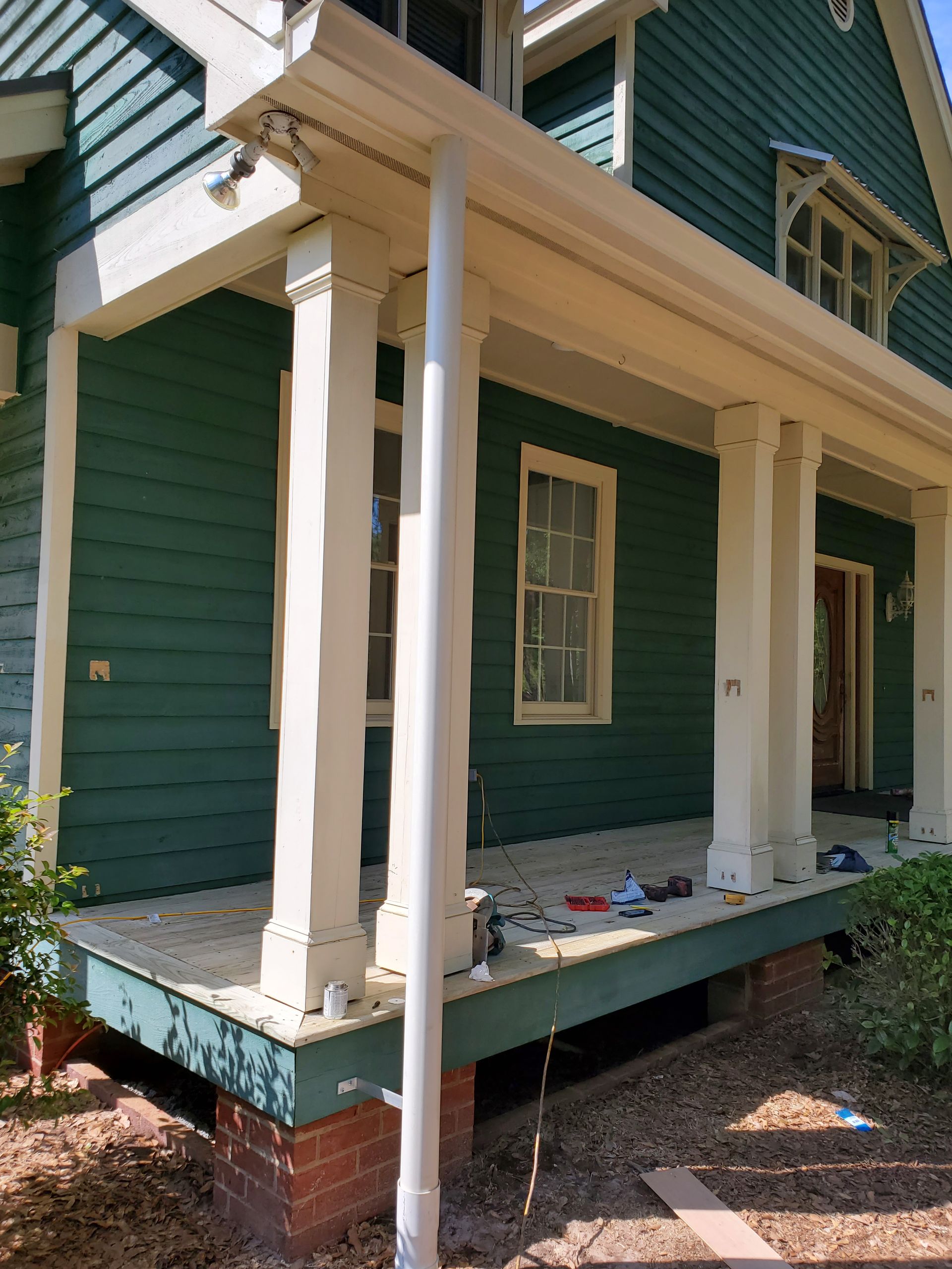 Green house with porch supported by white columns. White gutters and downspout visible.