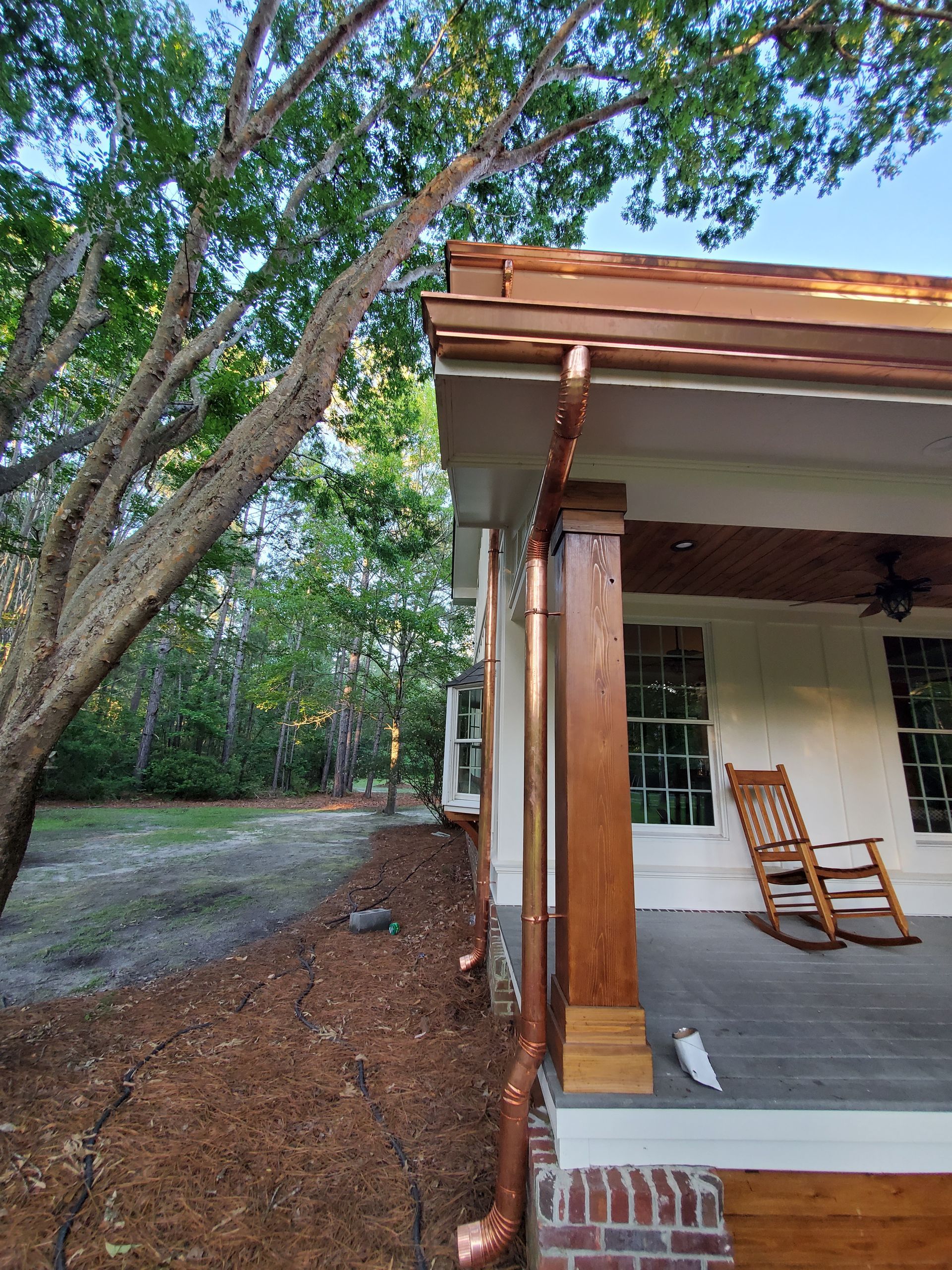 Copper gutters and downspouts on a house with a porch and rocking chairs.