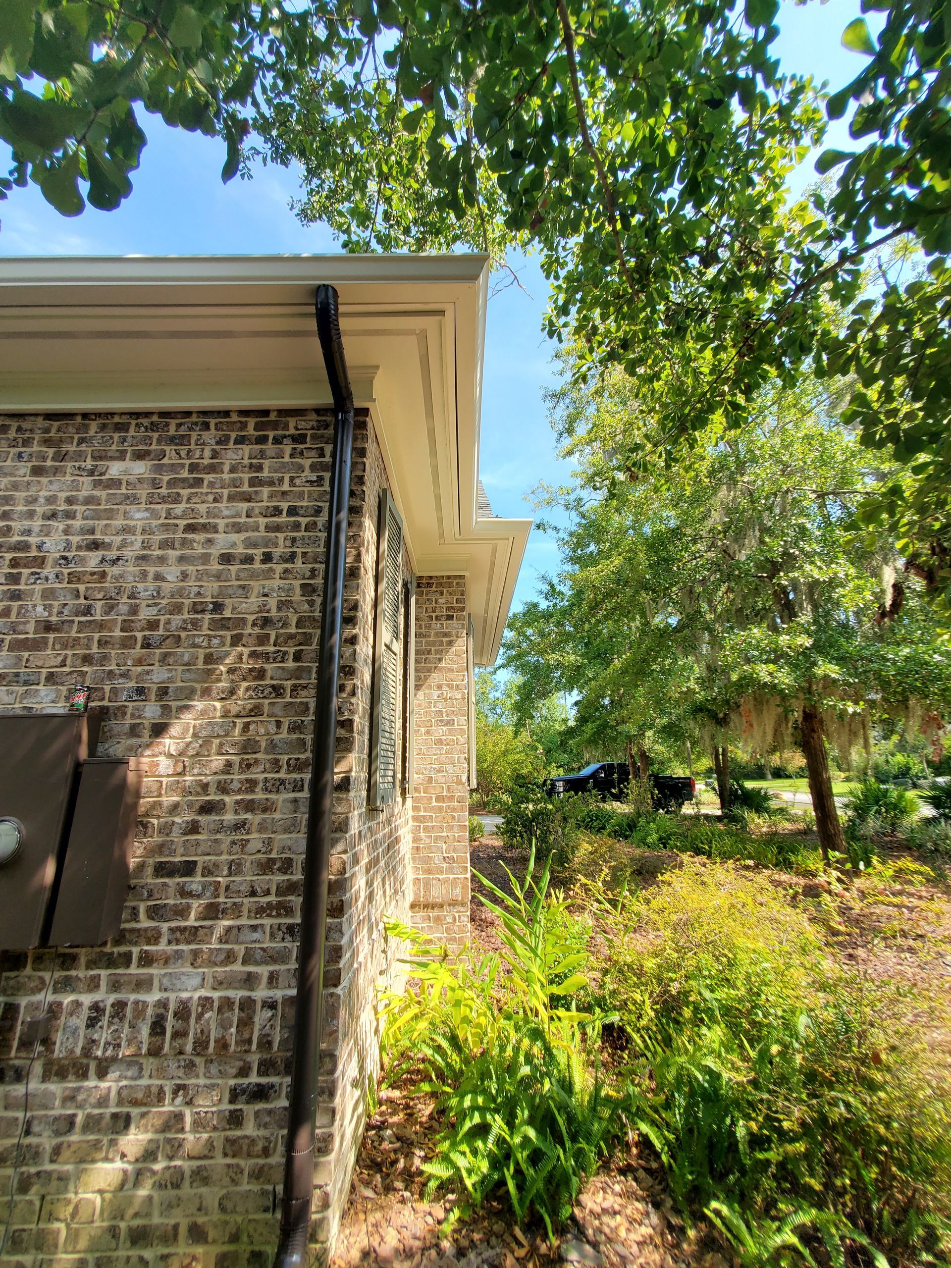 Brick building with black gutter and white trim, surrounded by green trees and foliage.